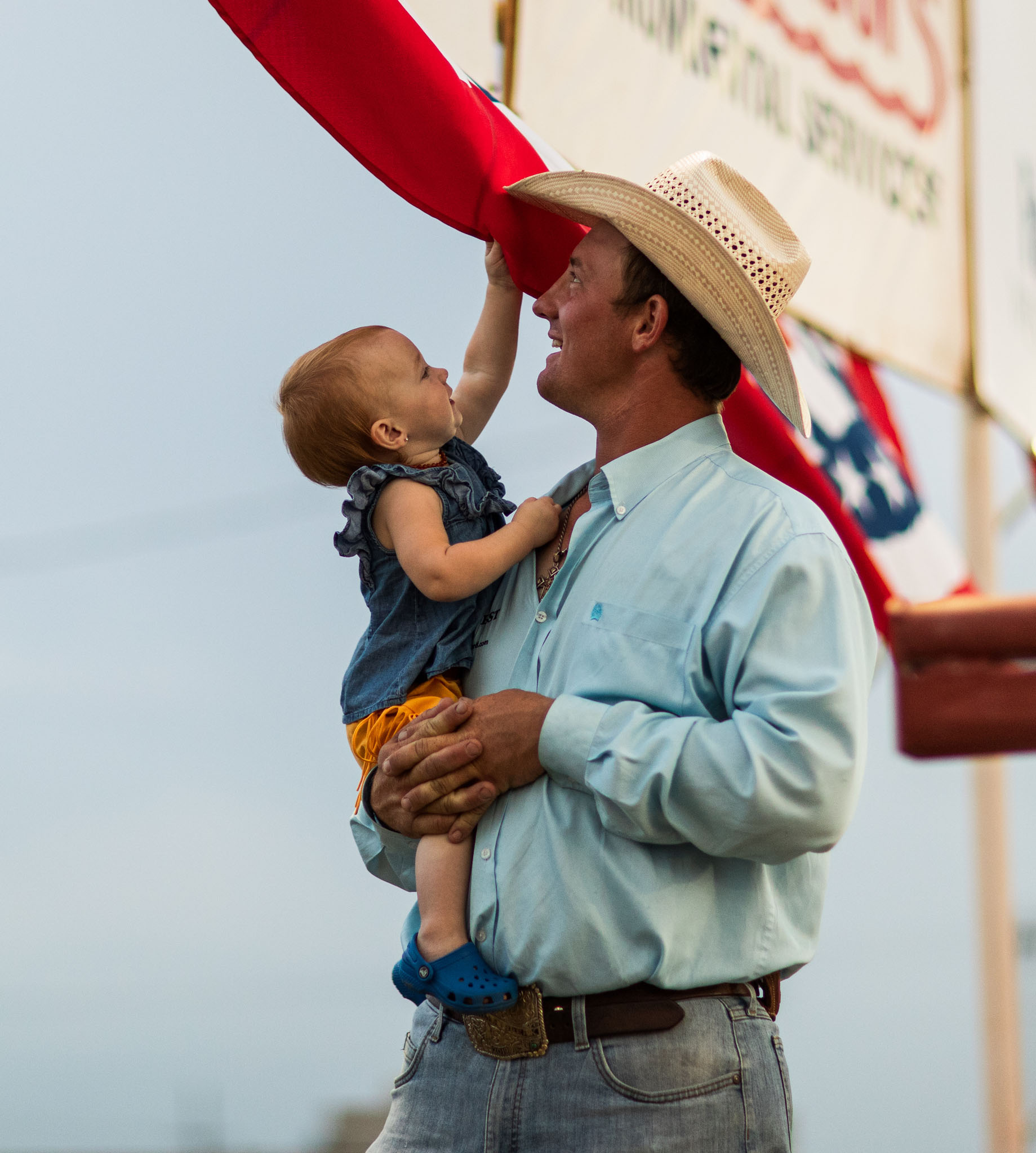 Father in a cowboy hat holding his young daughter beside the arena