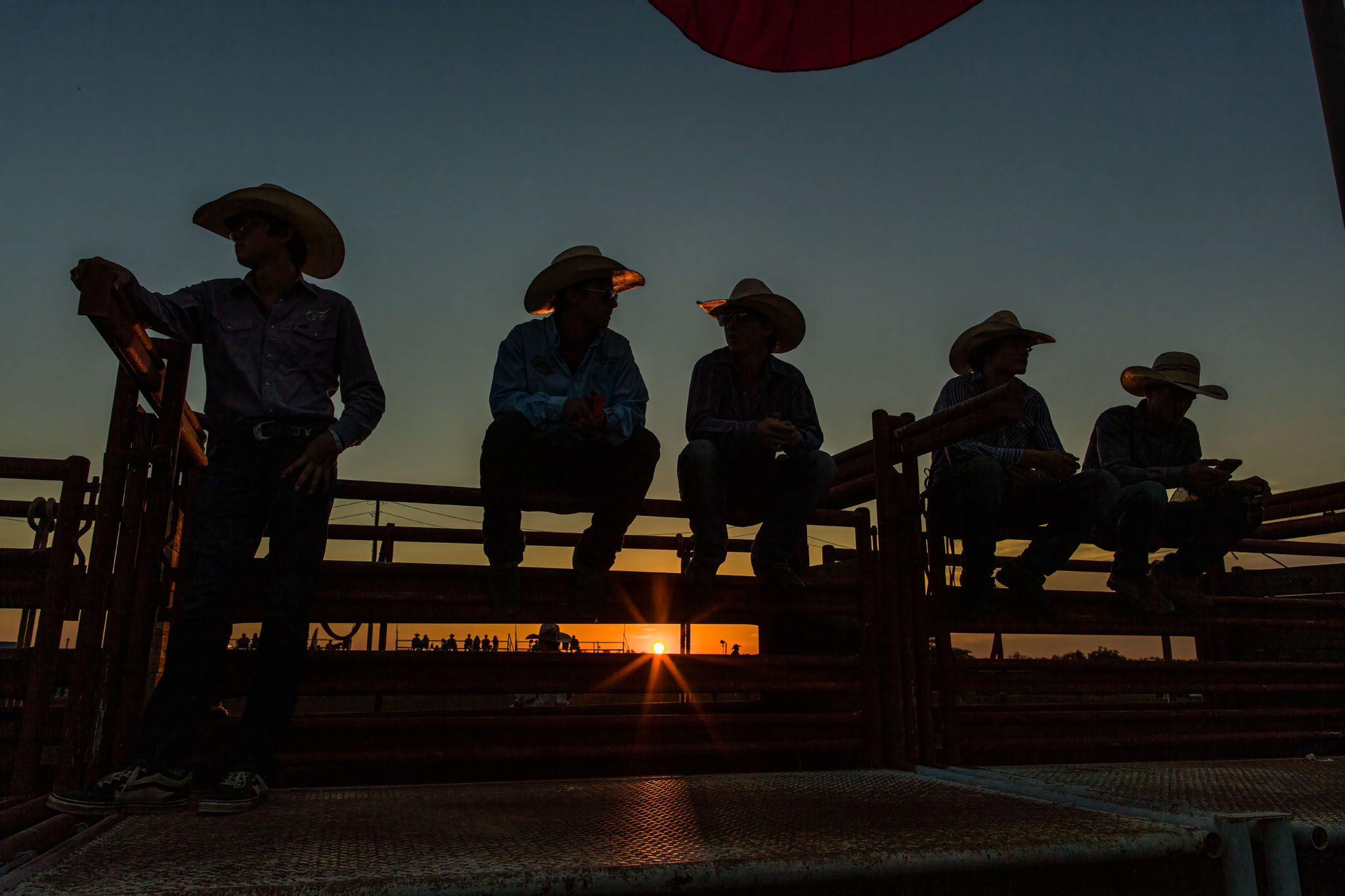 Cowboys silhouetted on the arena fence at sunset