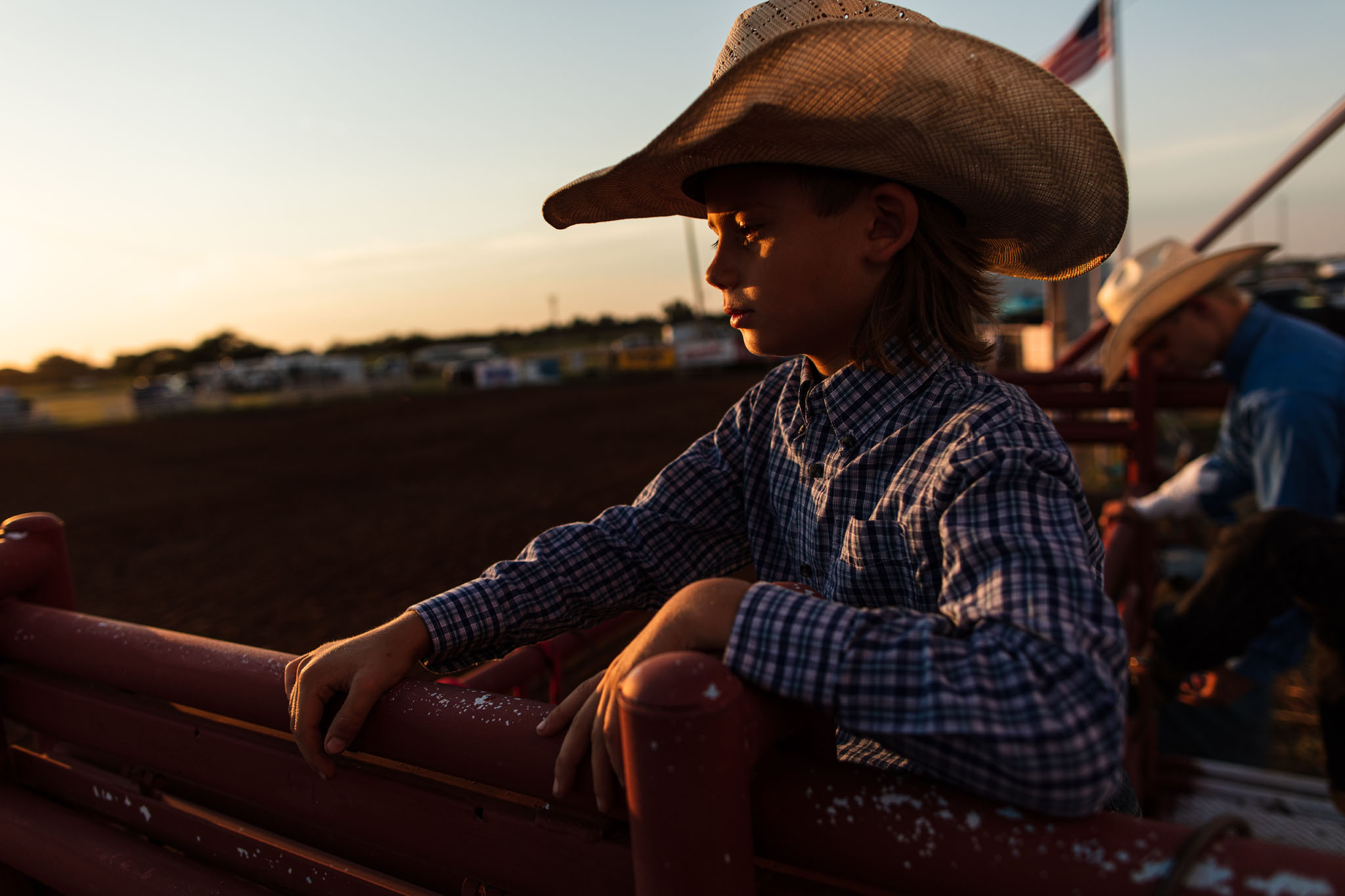 Cowboy leaning on the arena rail in golden evening light