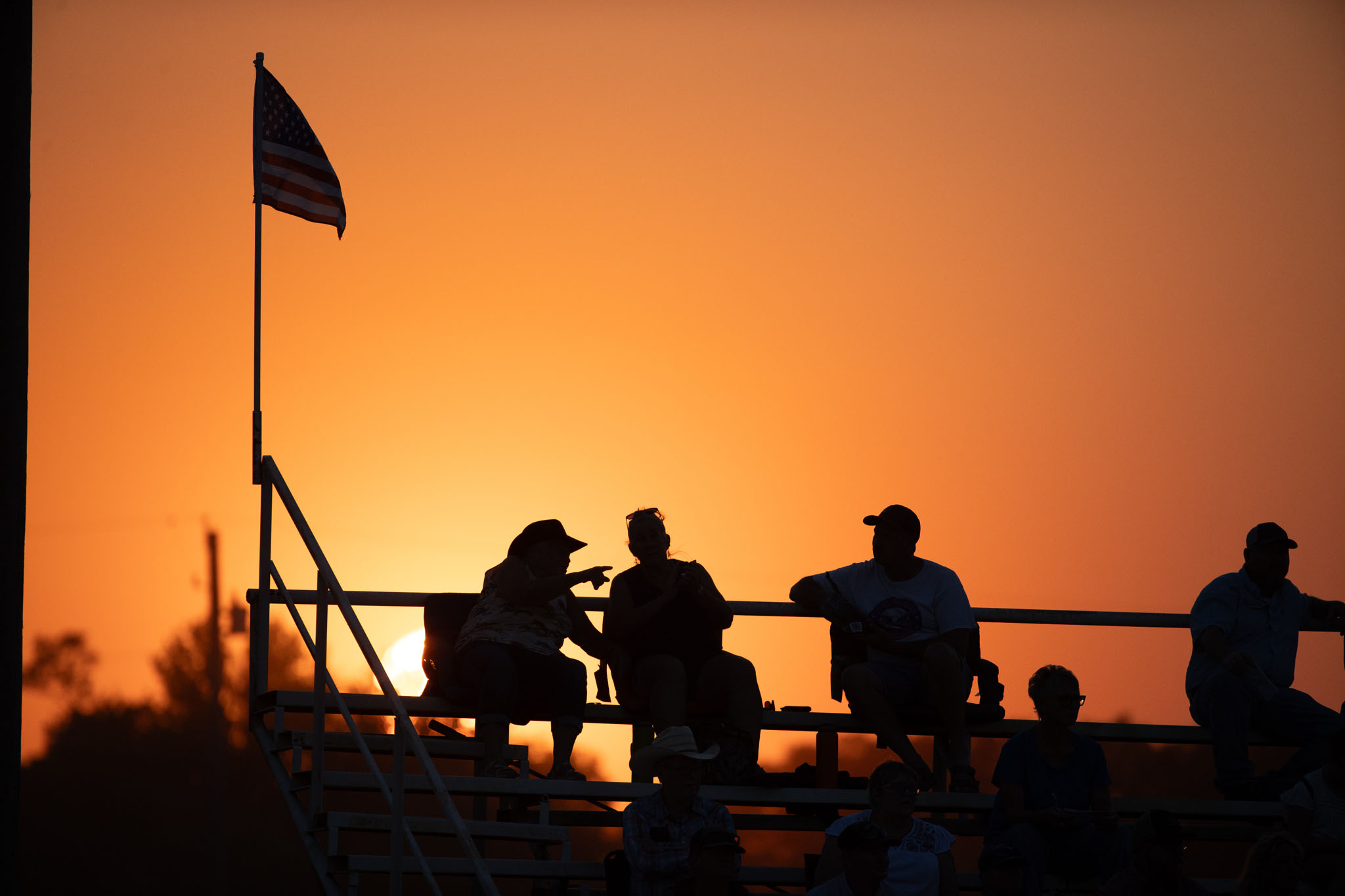 Spectators and a flag silhouetted against an orange sunset