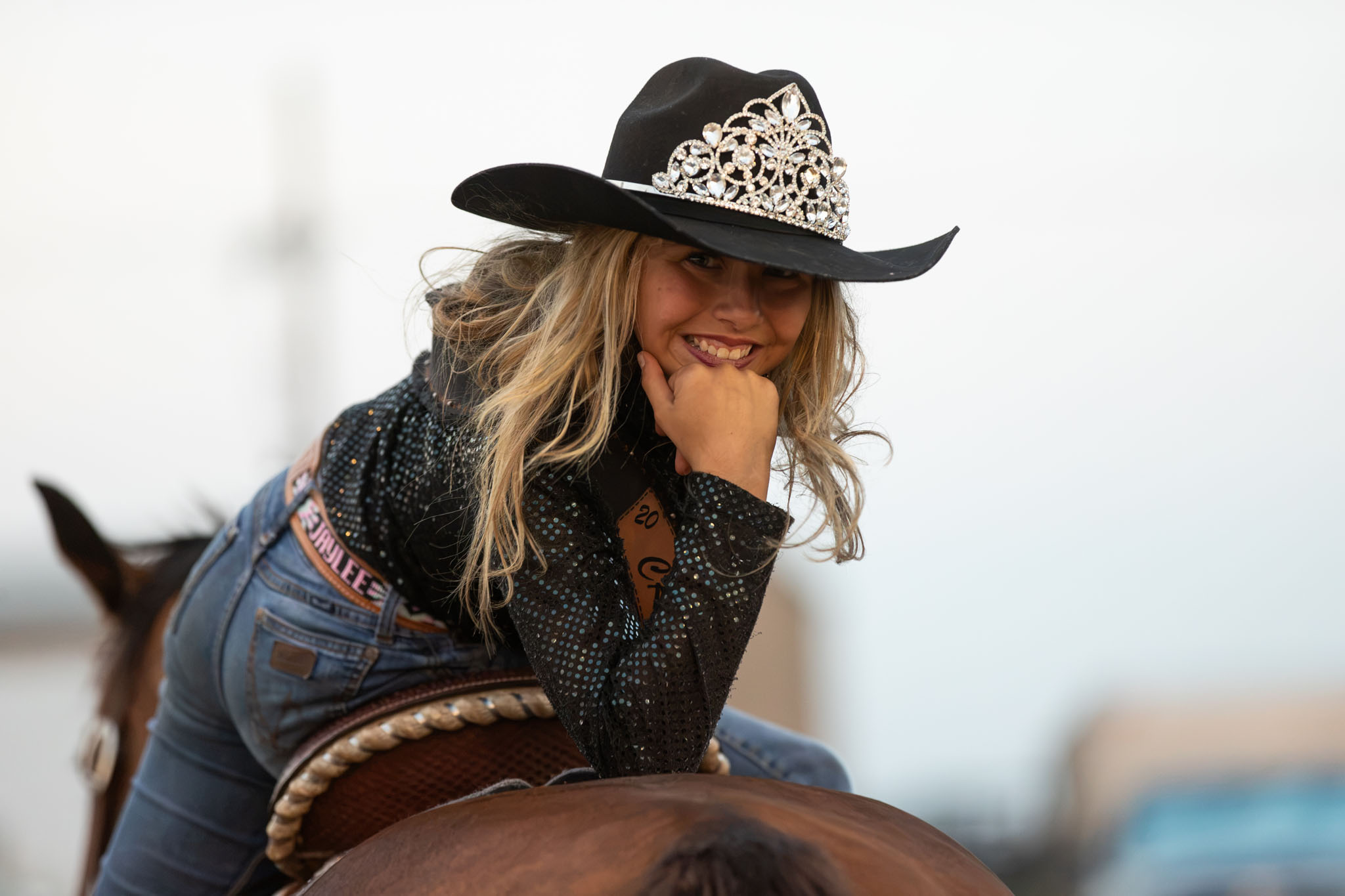 Rodeo queen in a sparkling hat leaning on her horse