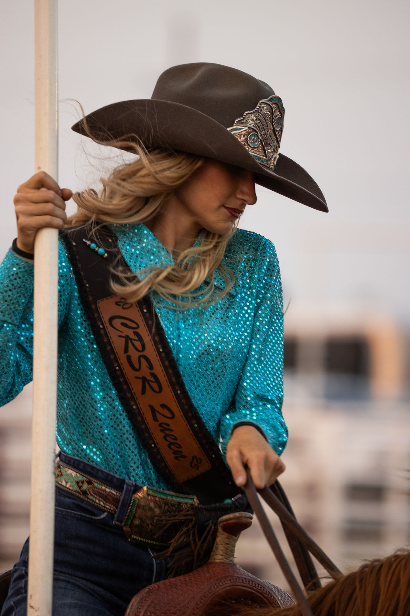 Cowgirl in a turquoise shirt holding a flag pole