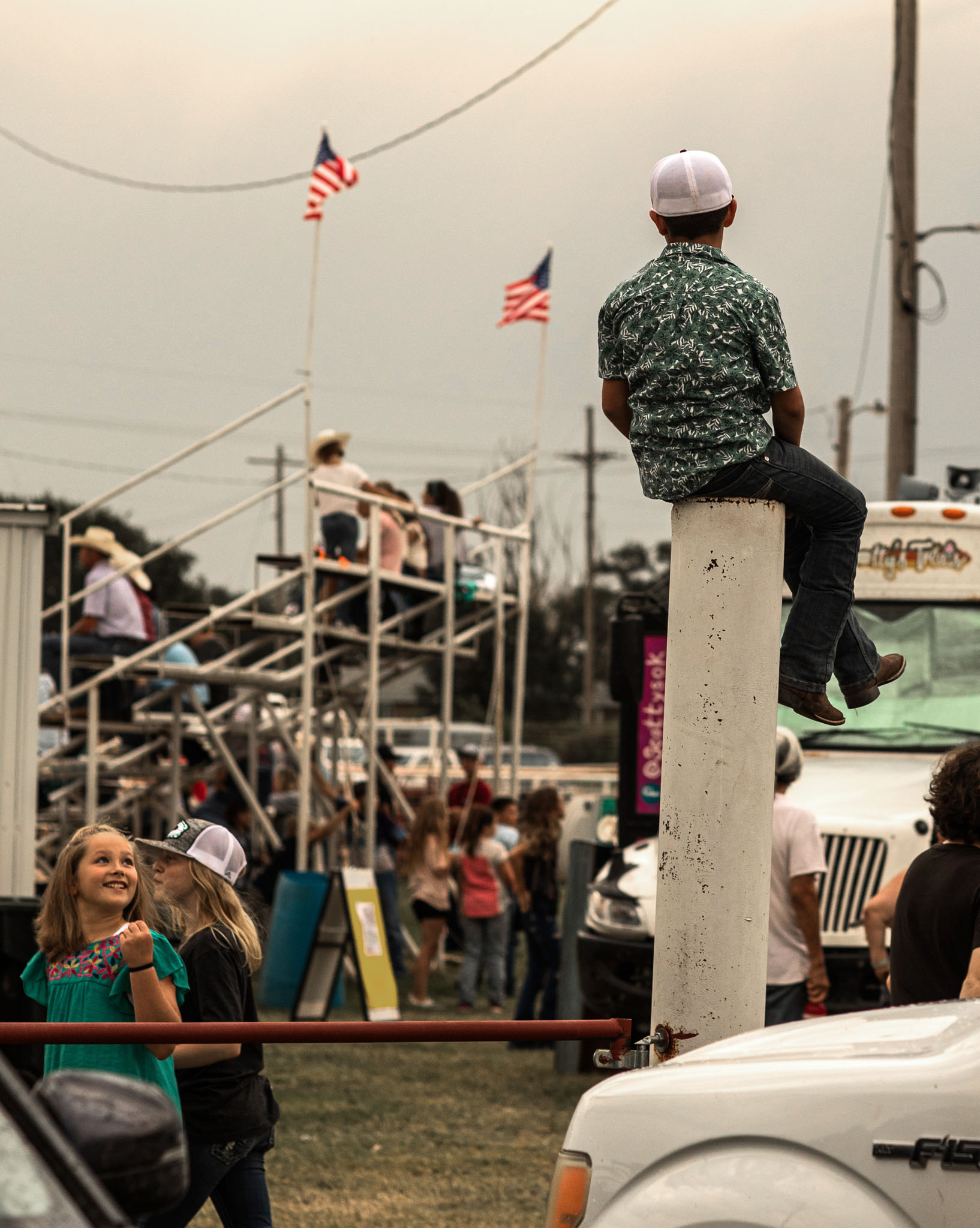 Boy perched on a fence post watching the crowd at the rodeo grounds