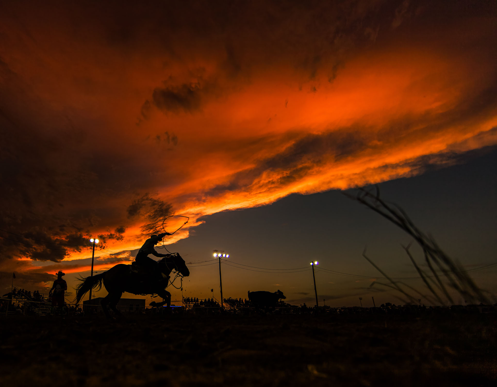 Lone rider silhouetted beneath a fiery orange sunset sky at the Cimarron River Stampede