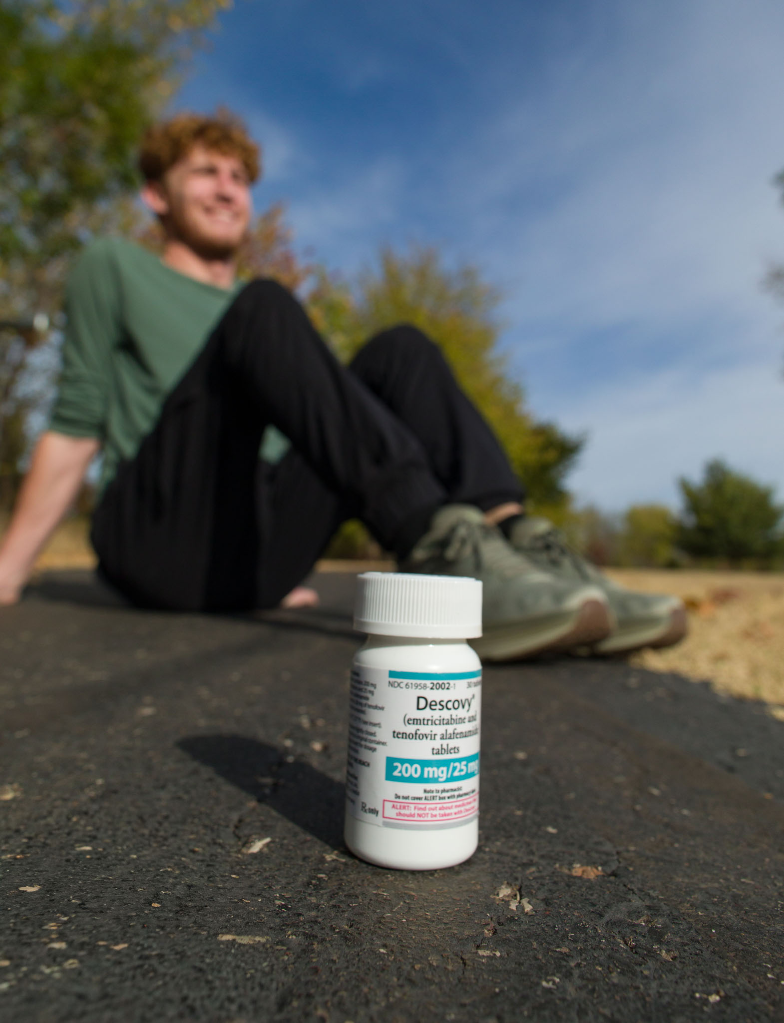 Young man sitting on a path with a prescription bottle in the foreground