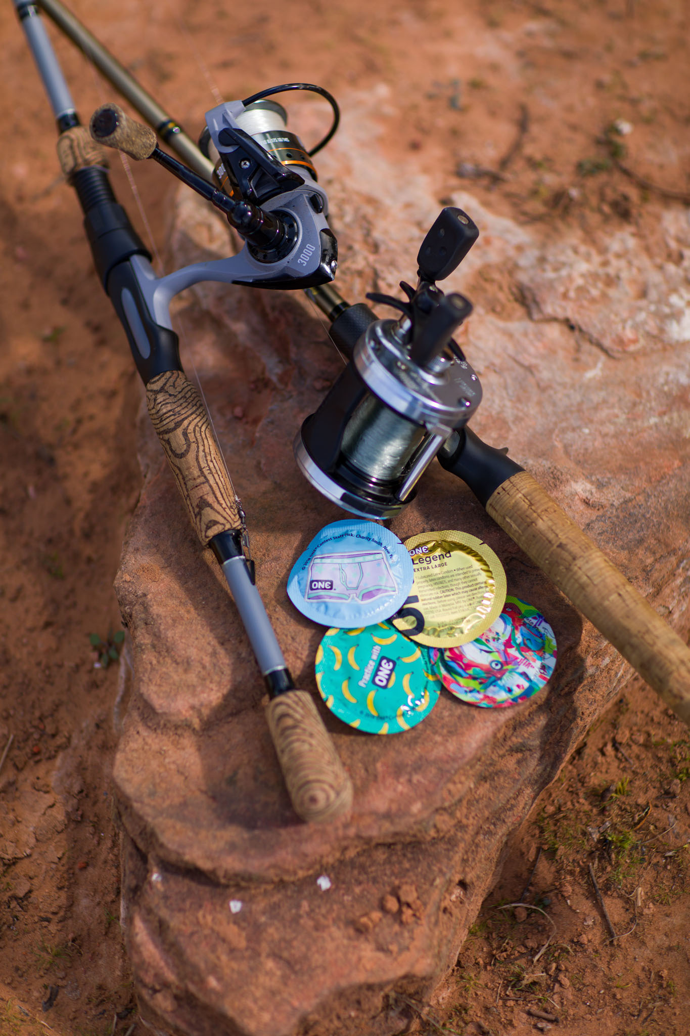 Fishing rod and reel resting on red rock beside colorful buttons