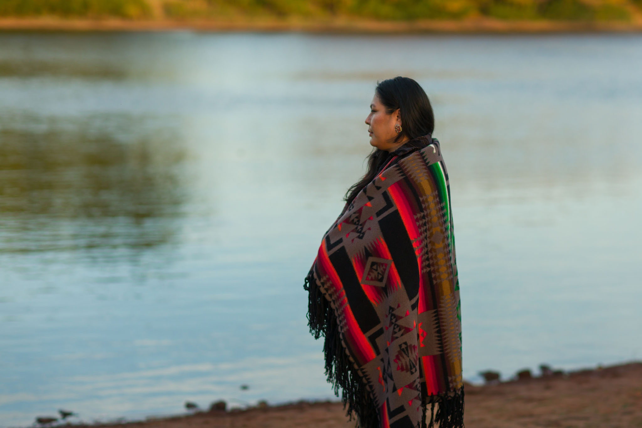 Woman in a patterned blanket looking out over a lake