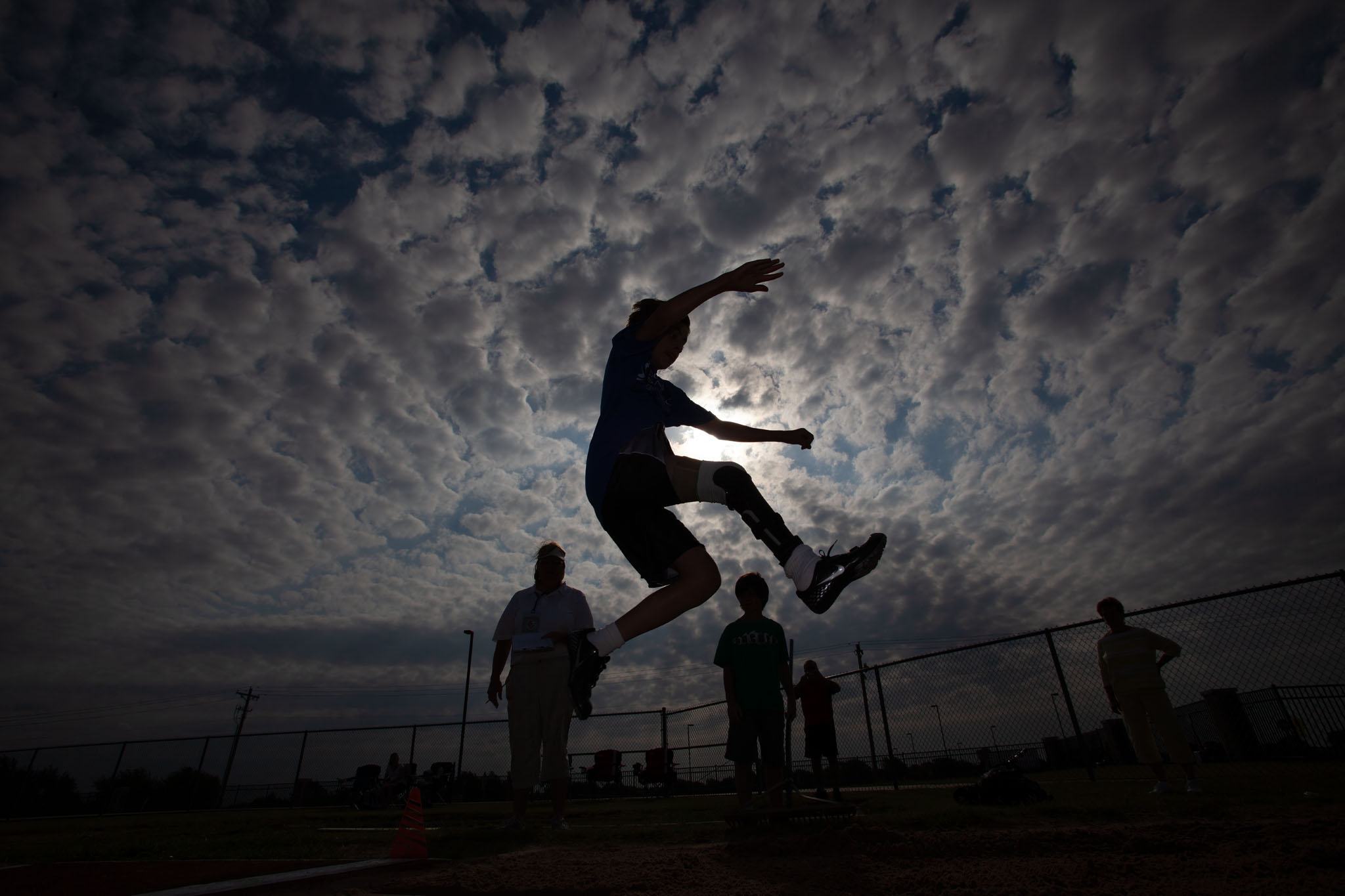 High jumper silhouetted mid-air against a dramatic cloudy sky