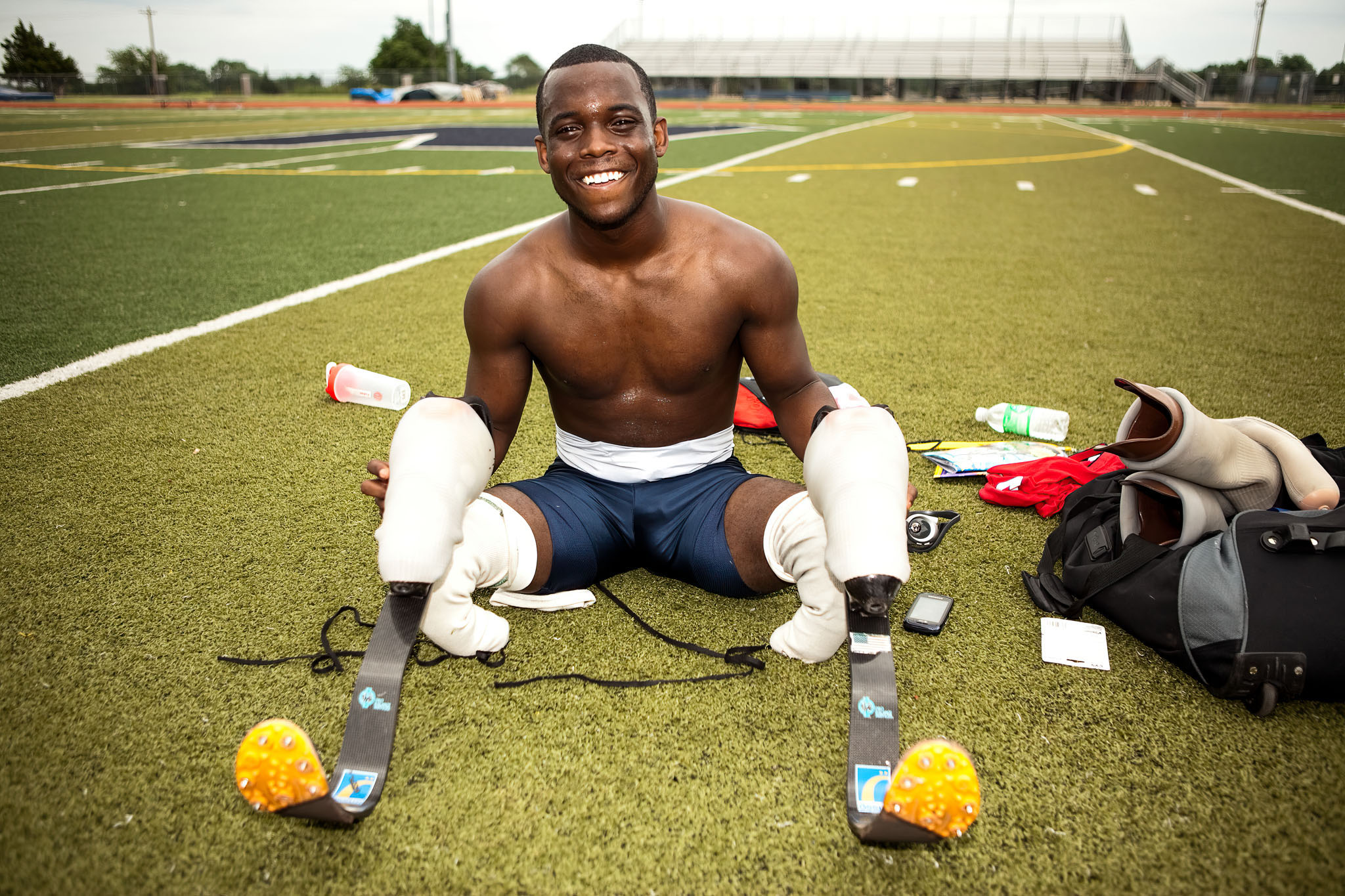 Smiling athlete seated on the turf with his prosthetic legs beside him