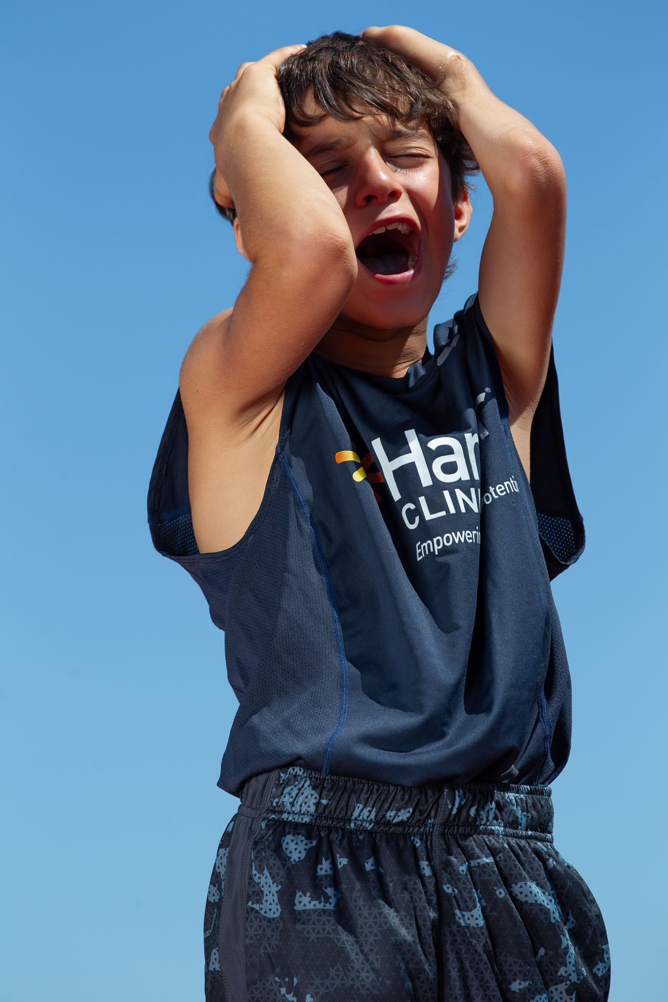 Boy shouting with joy, his hands on his head, under a blue sky