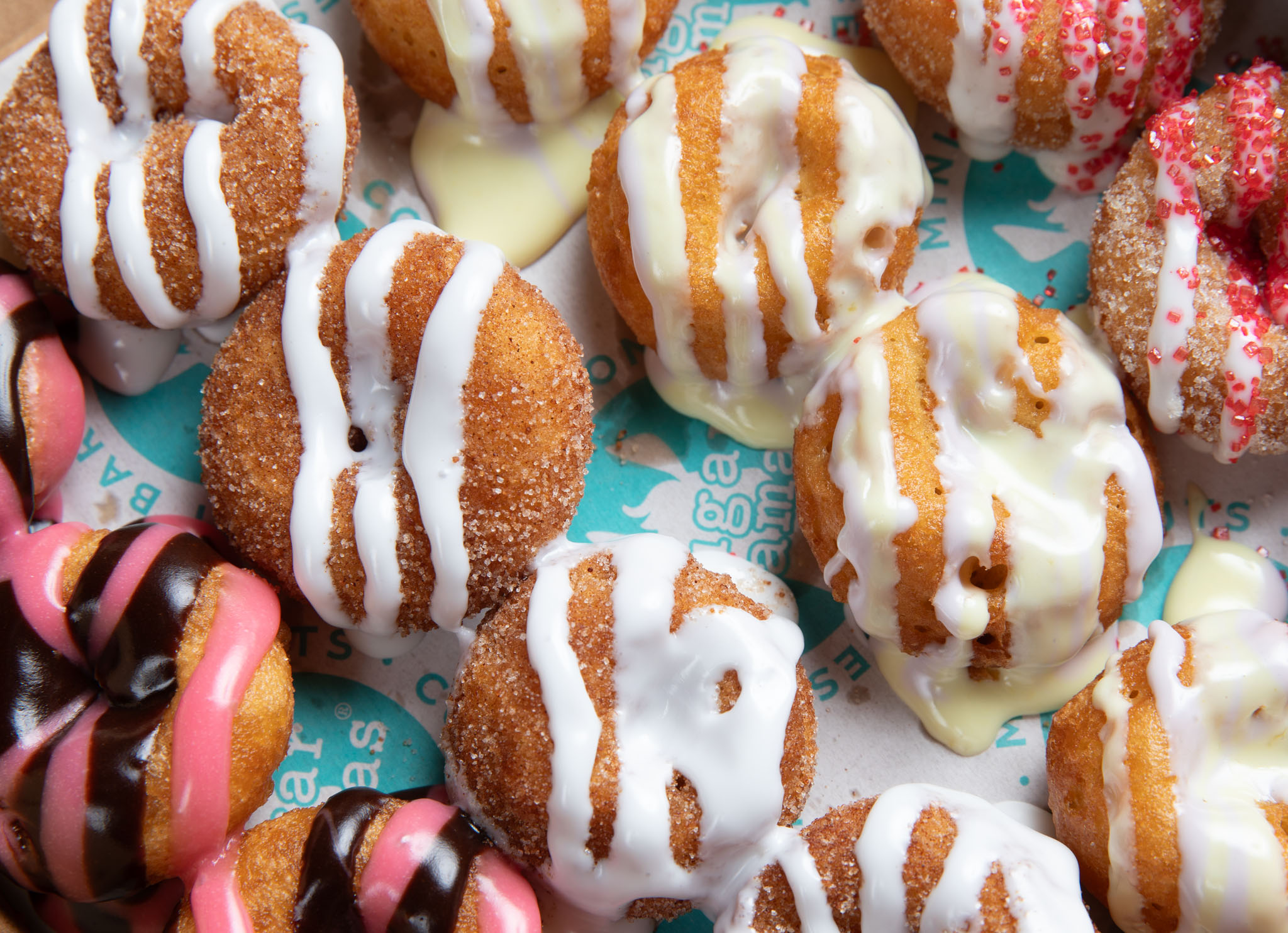 Cinnamon-sugar doughnuts drizzled with white icing alongside pink and chocolate-glazed doughnuts
