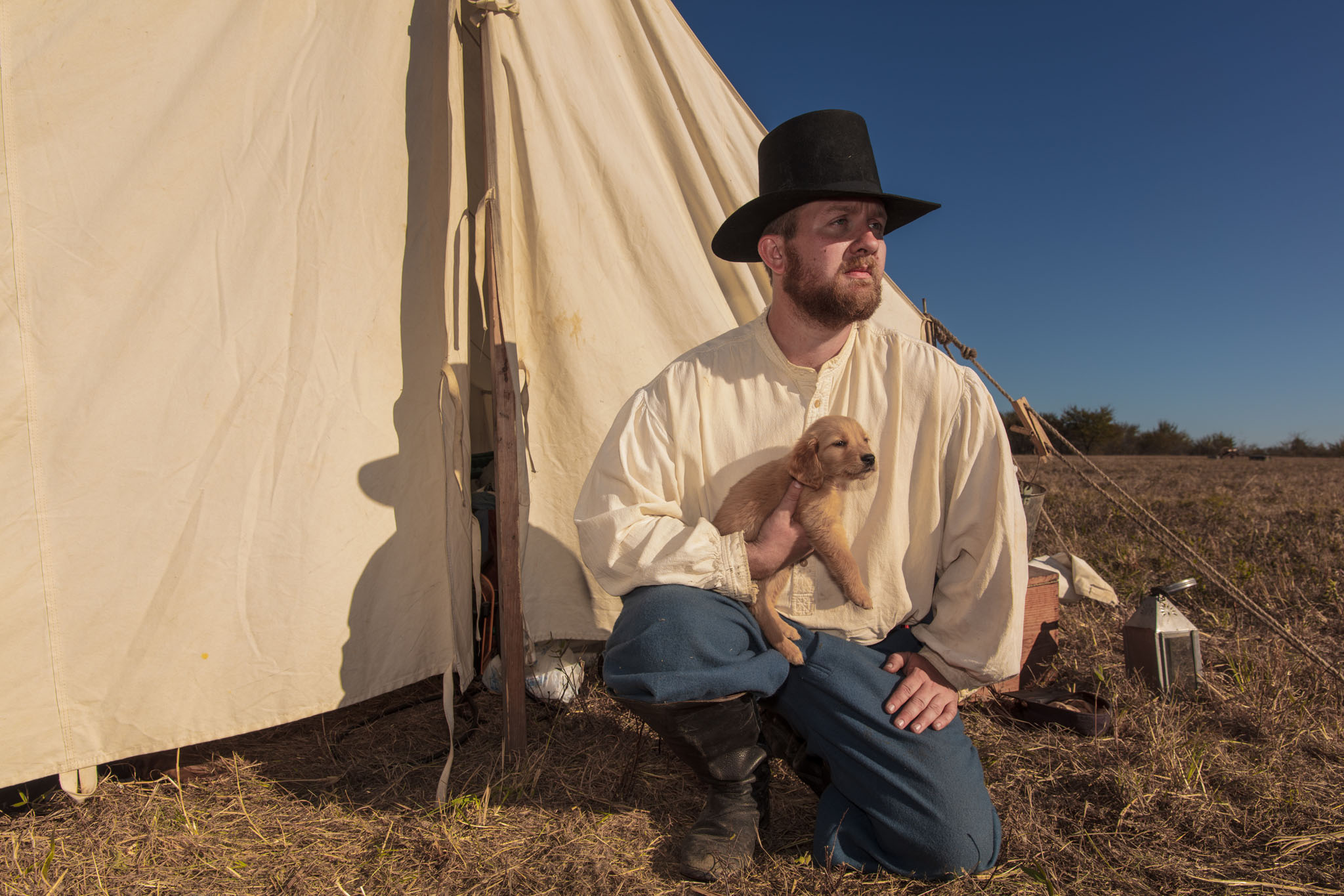 Reenactor kneeling outside his tent holding a puppy