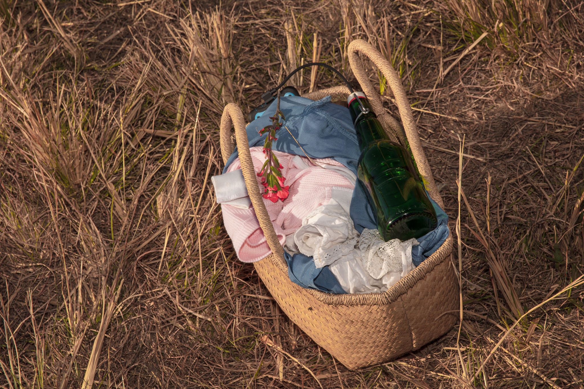 Woven basket of linens and bottles resting in the grass
