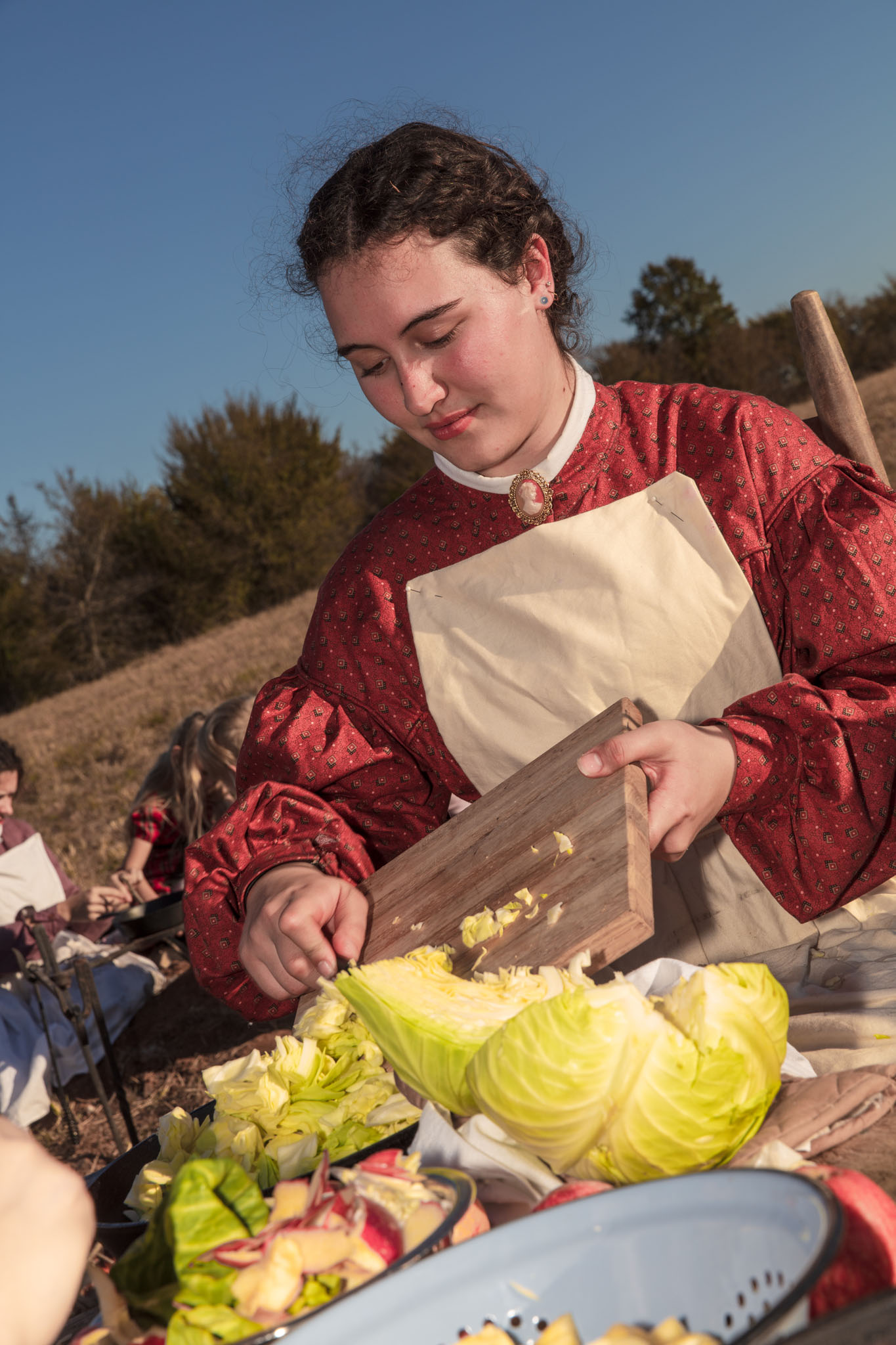 Young woman in a red dress chopping cabbage for a camp meal