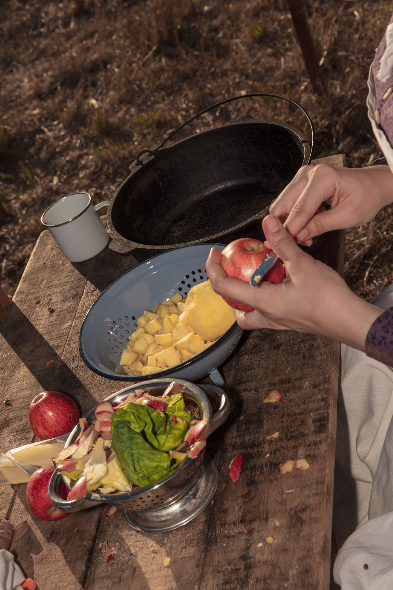 Hands slicing apples beside a bowl of potatoes