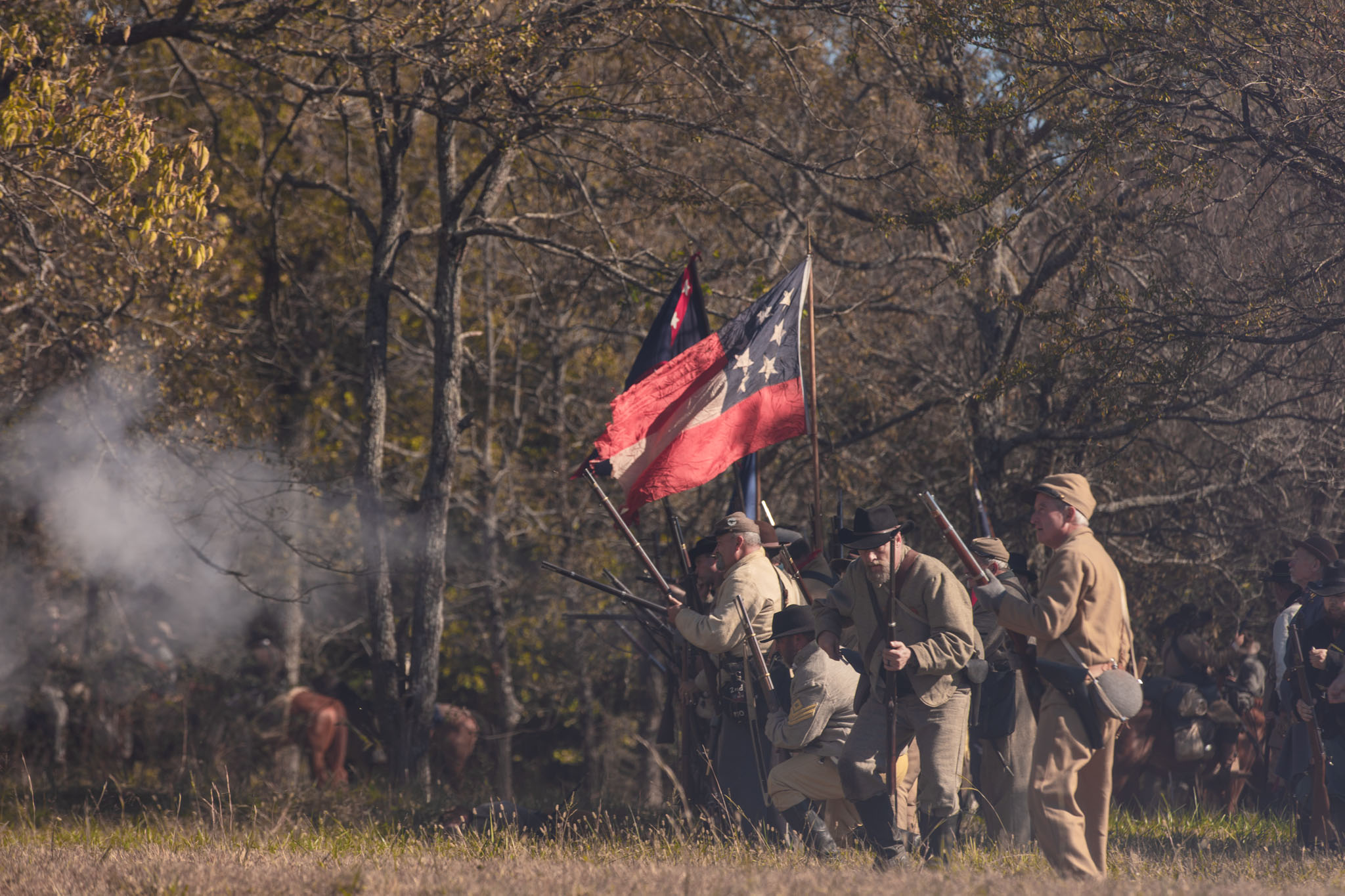 Confederate soldiers advancing through the trees with their battle flag