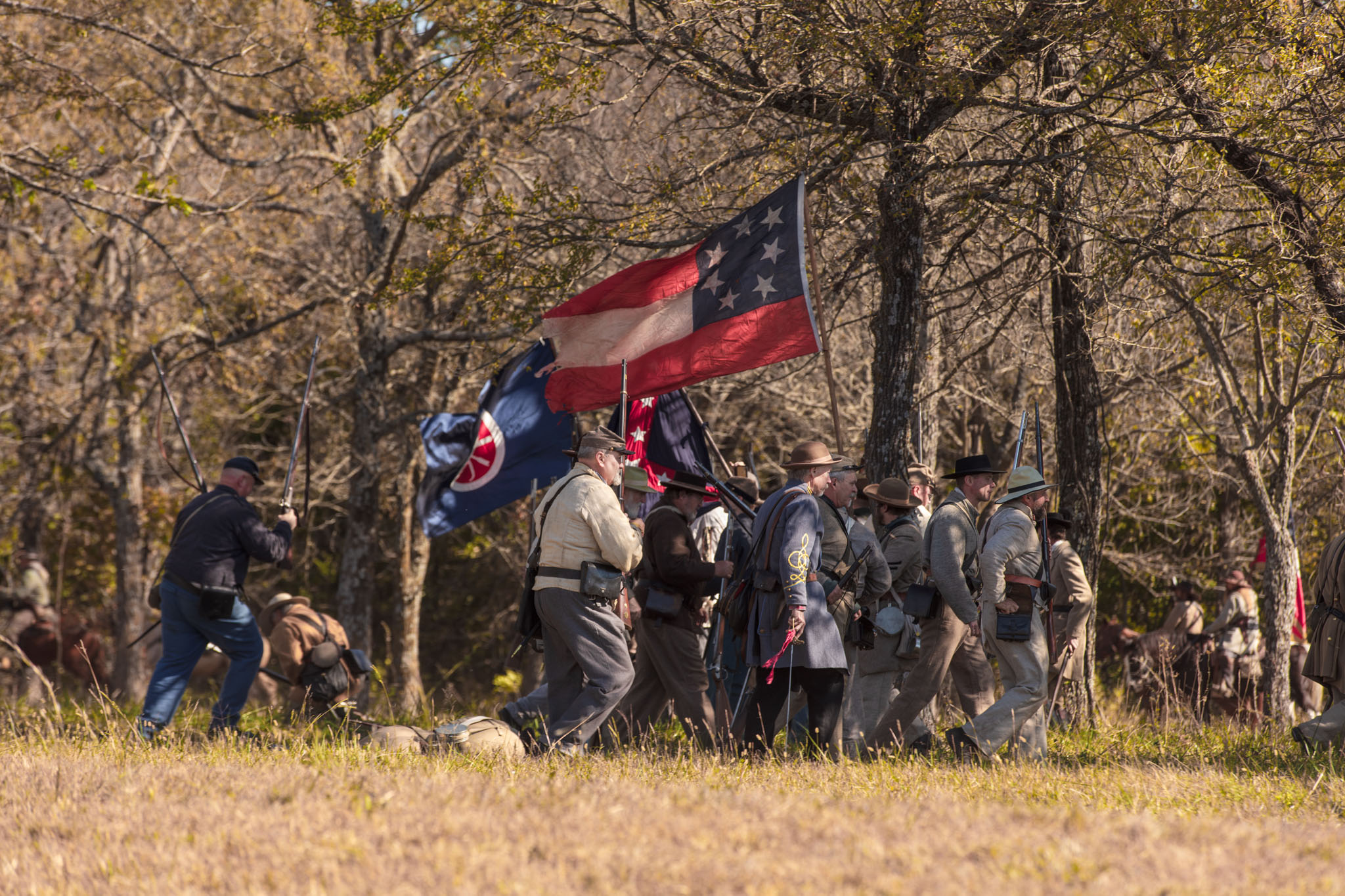 Confederate soldiers gathered beneath battle flags at the edge of the woods