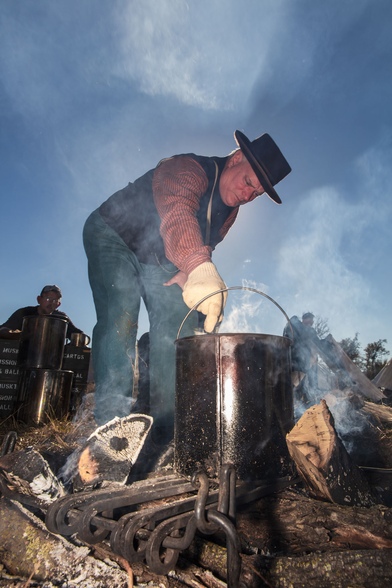 Reenactor tending a cook pot over a smoky campfire
