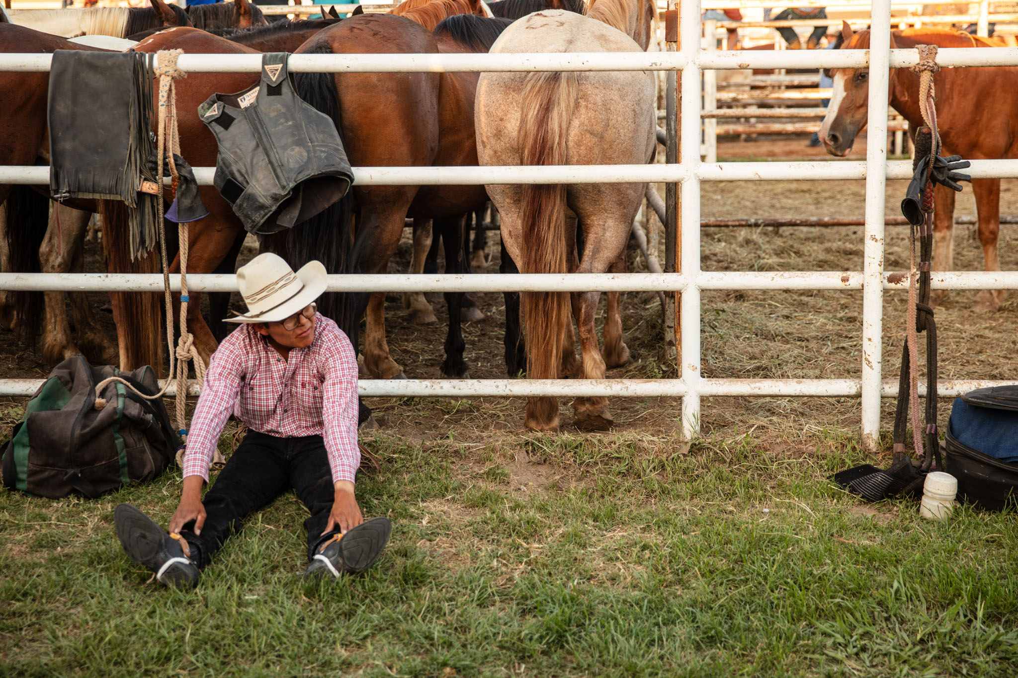 Cowboy sitting in the grass beside the horse pens before his event