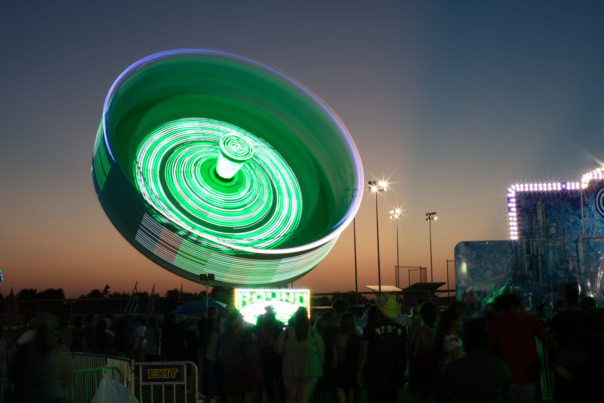 Spinning carnival ride lit in green at dusk