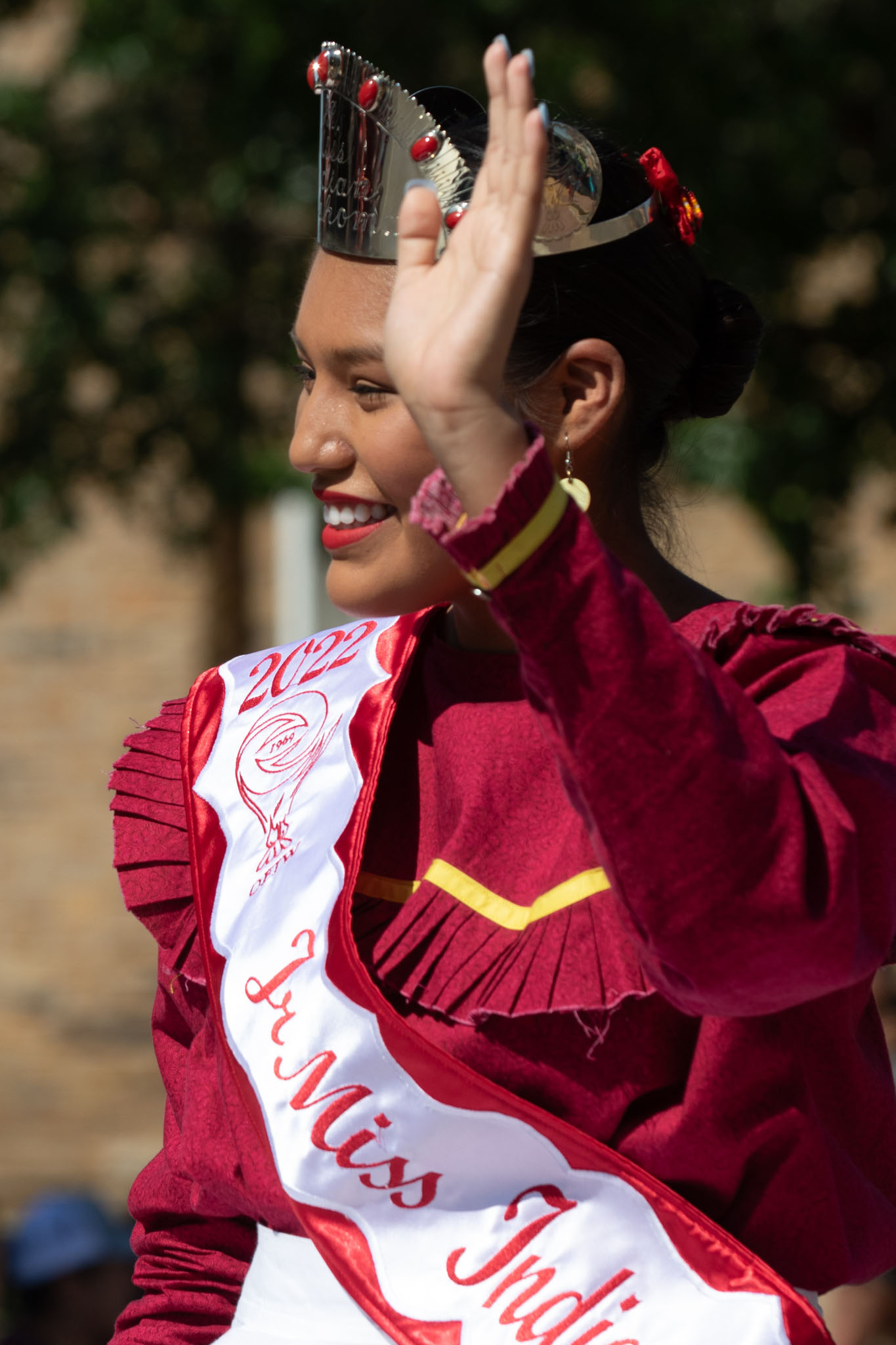 Festival royalty in a crown and sash waving during the parade
