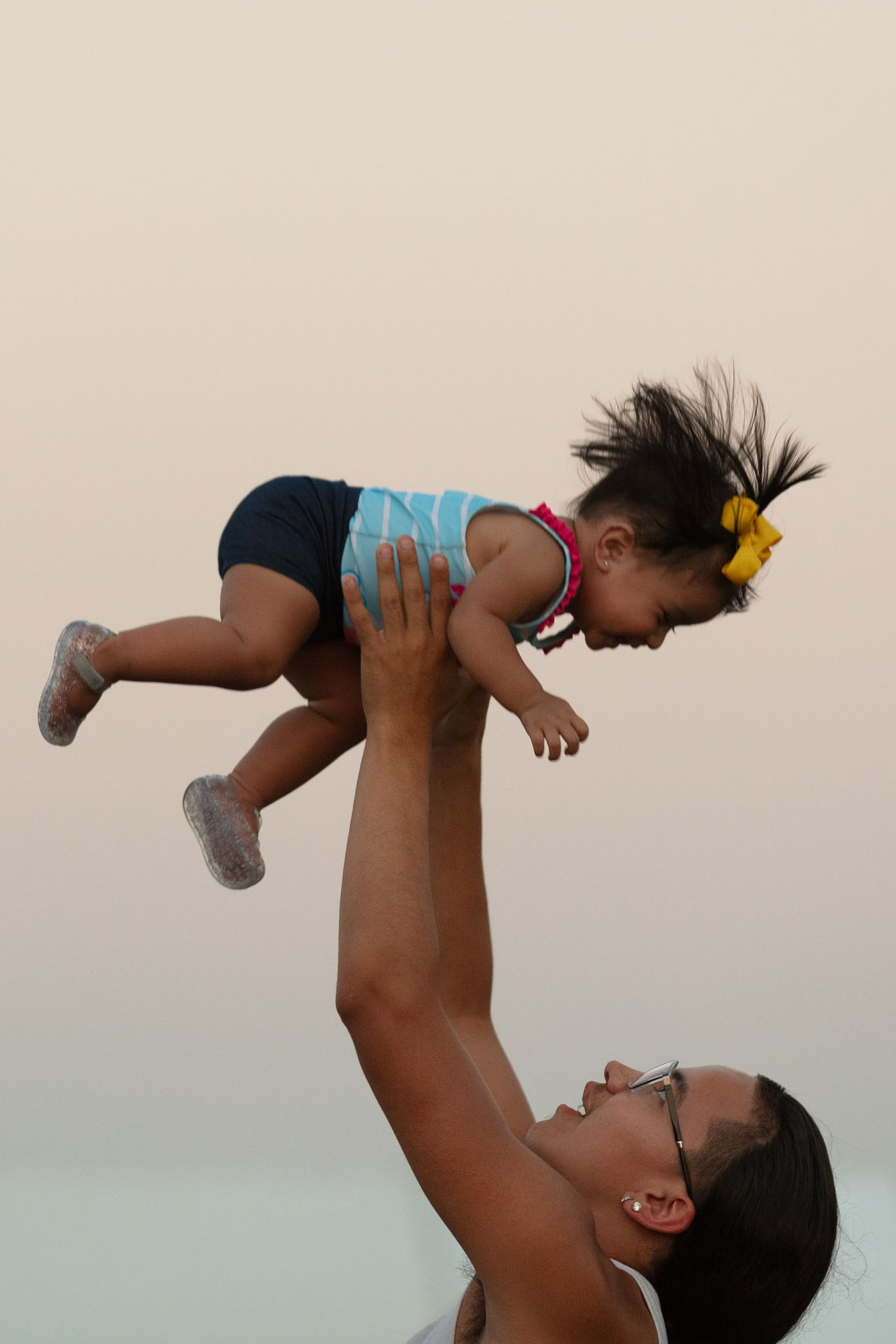 Mother lifting her young daughter into the air at dusk