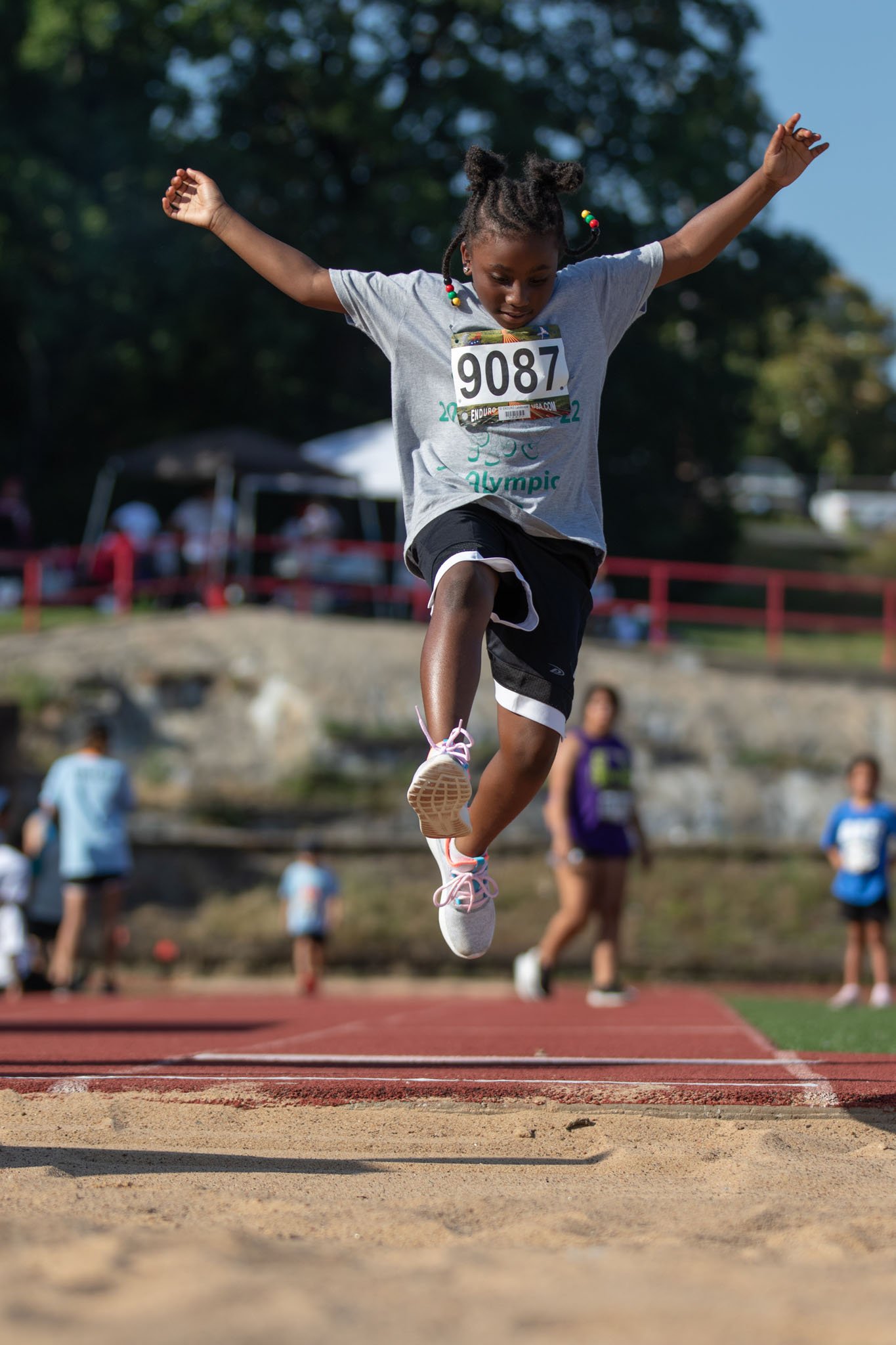 Young athlete in a race bib leaping into the long jump pit