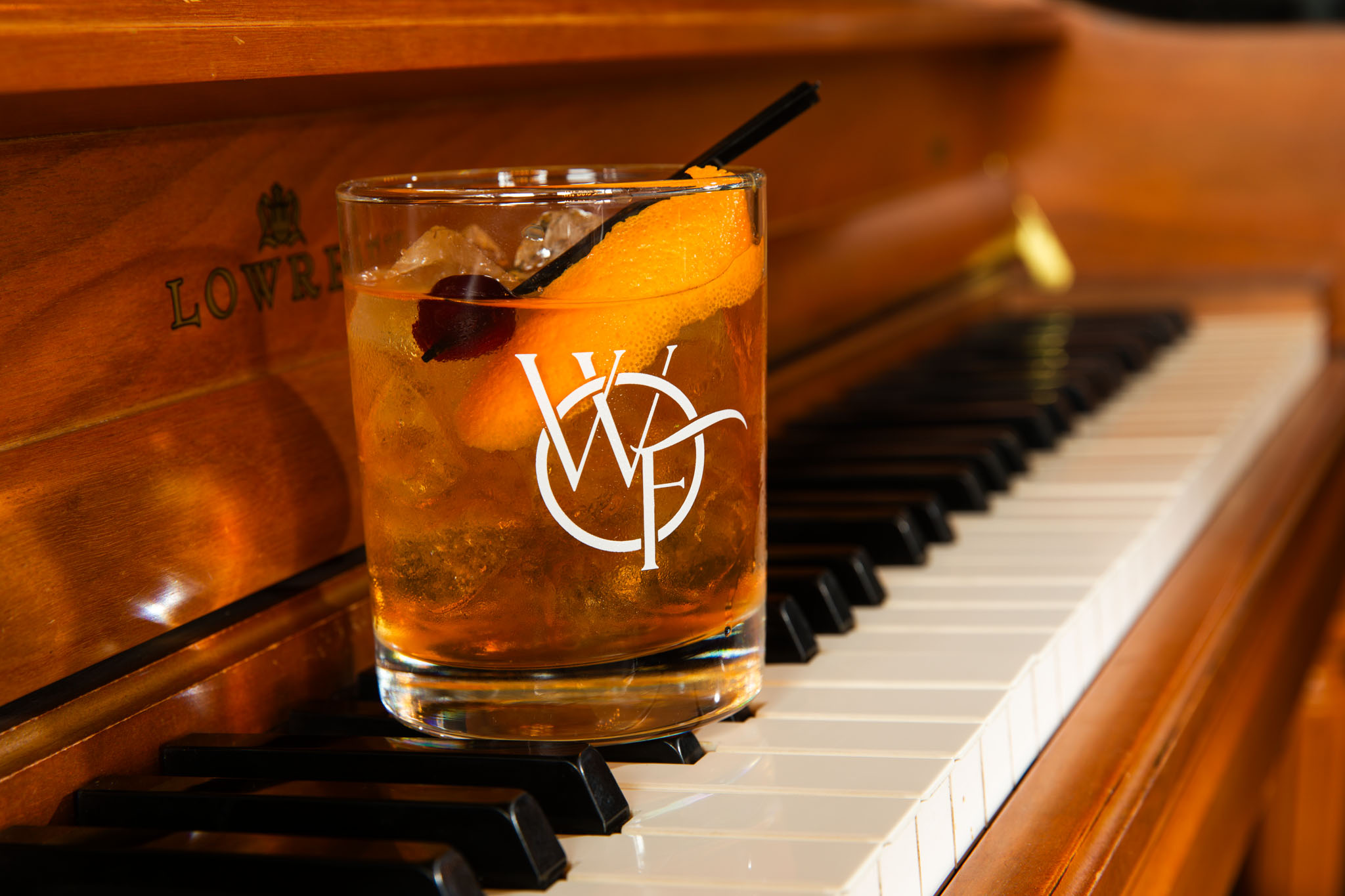 Amber cocktail with an orange peel and cherry in a monogrammed glass resting on piano keys