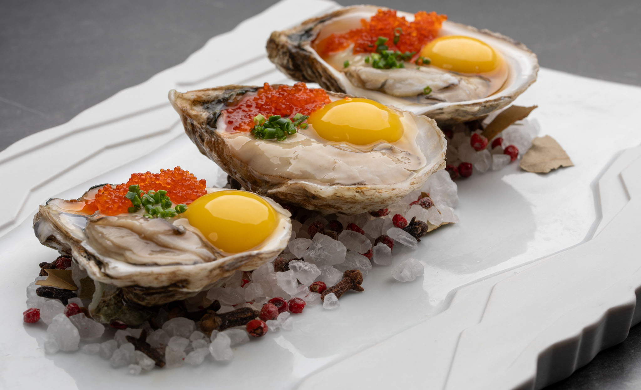 Oysters on the half shell topped with orange roe, chives and quail egg yolks, served on rock salt and pink peppercorns