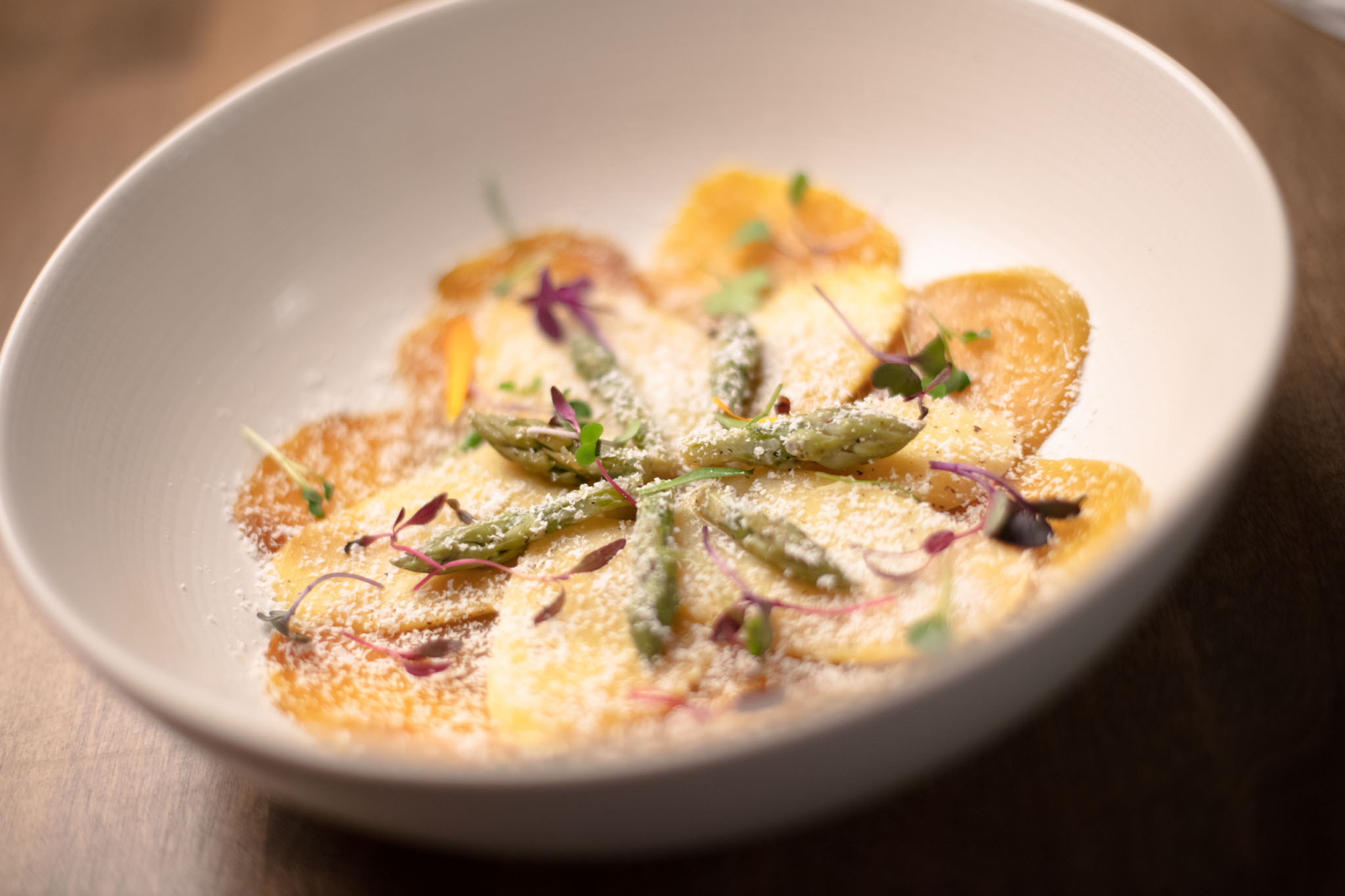 Shallow white bowl of golden rounds topped with asparagus tips, microgreens and a dusting of grated cheese