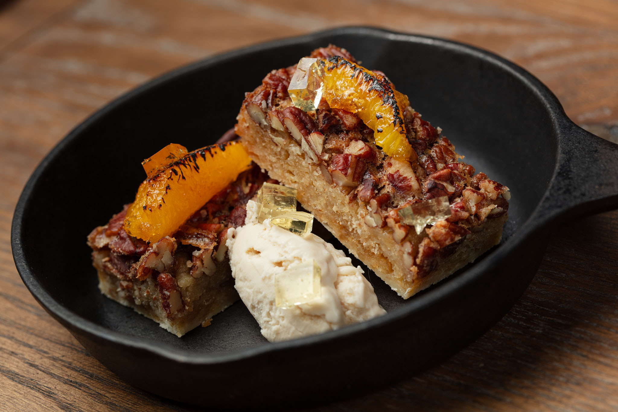 Pecan dessert bar topped with charred orange segments and a scoop of ice cream, served in a small cast-iron skillet