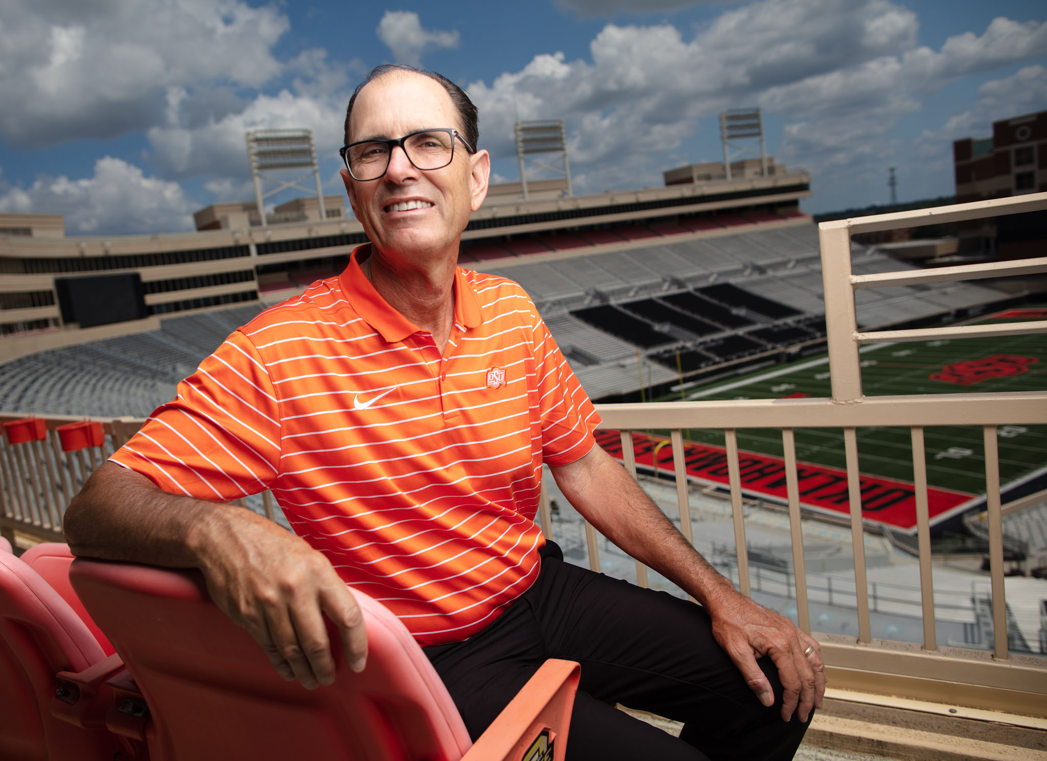 Man in an orange polo seated in the red seats of a stadium