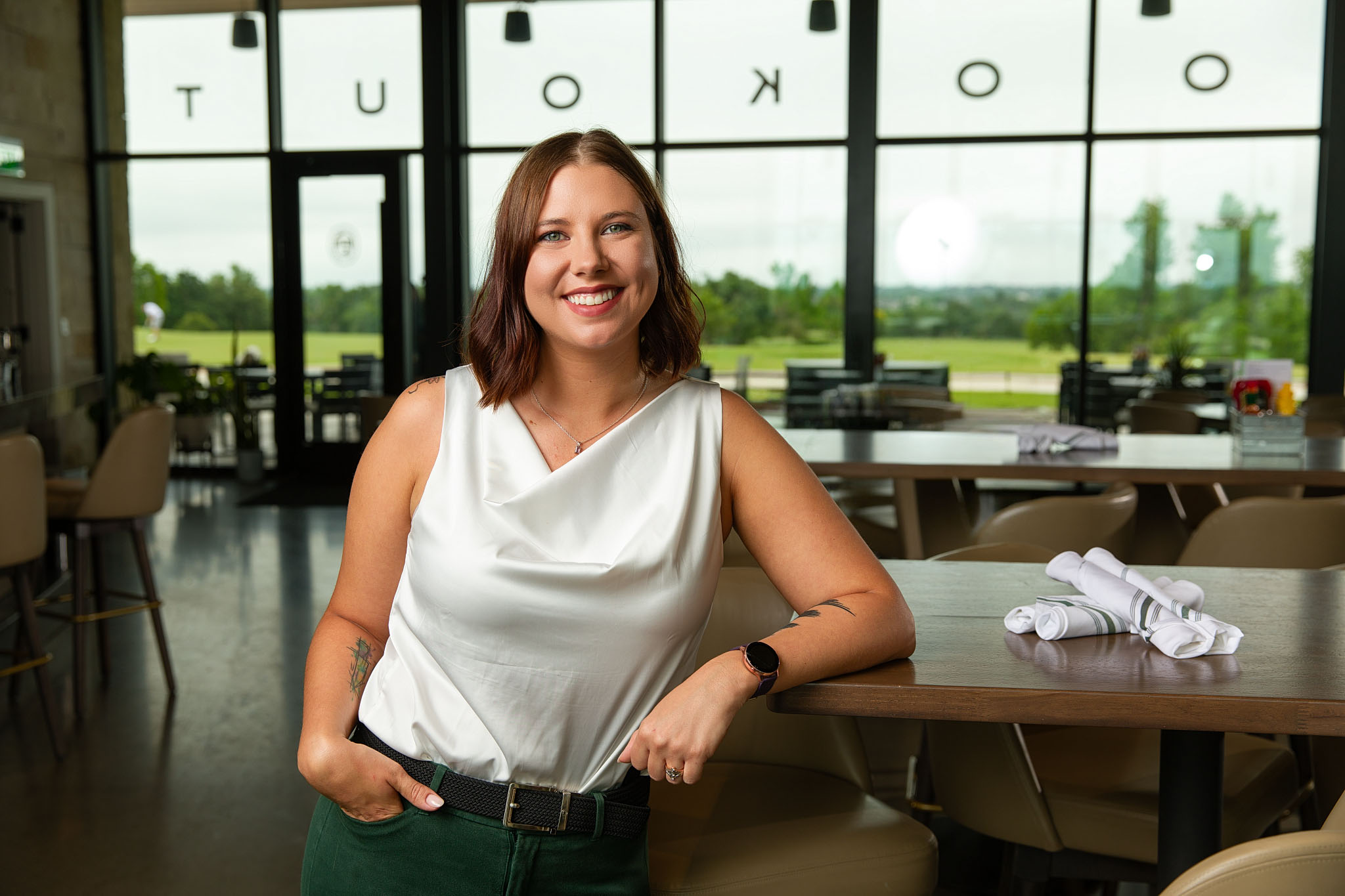 Smiling woman in a white top standing in a restaurant with large windows