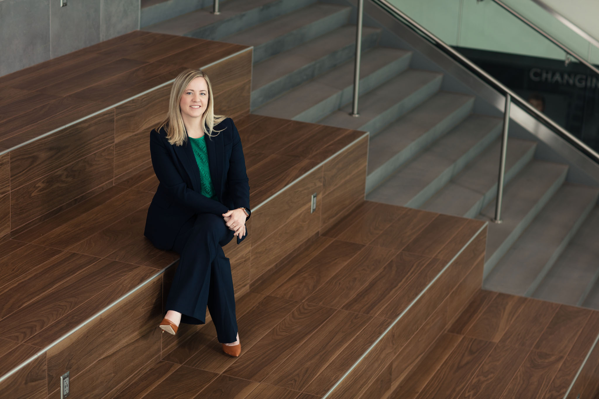 Woman in a dark suit seated on wide wooden steps in a modern building