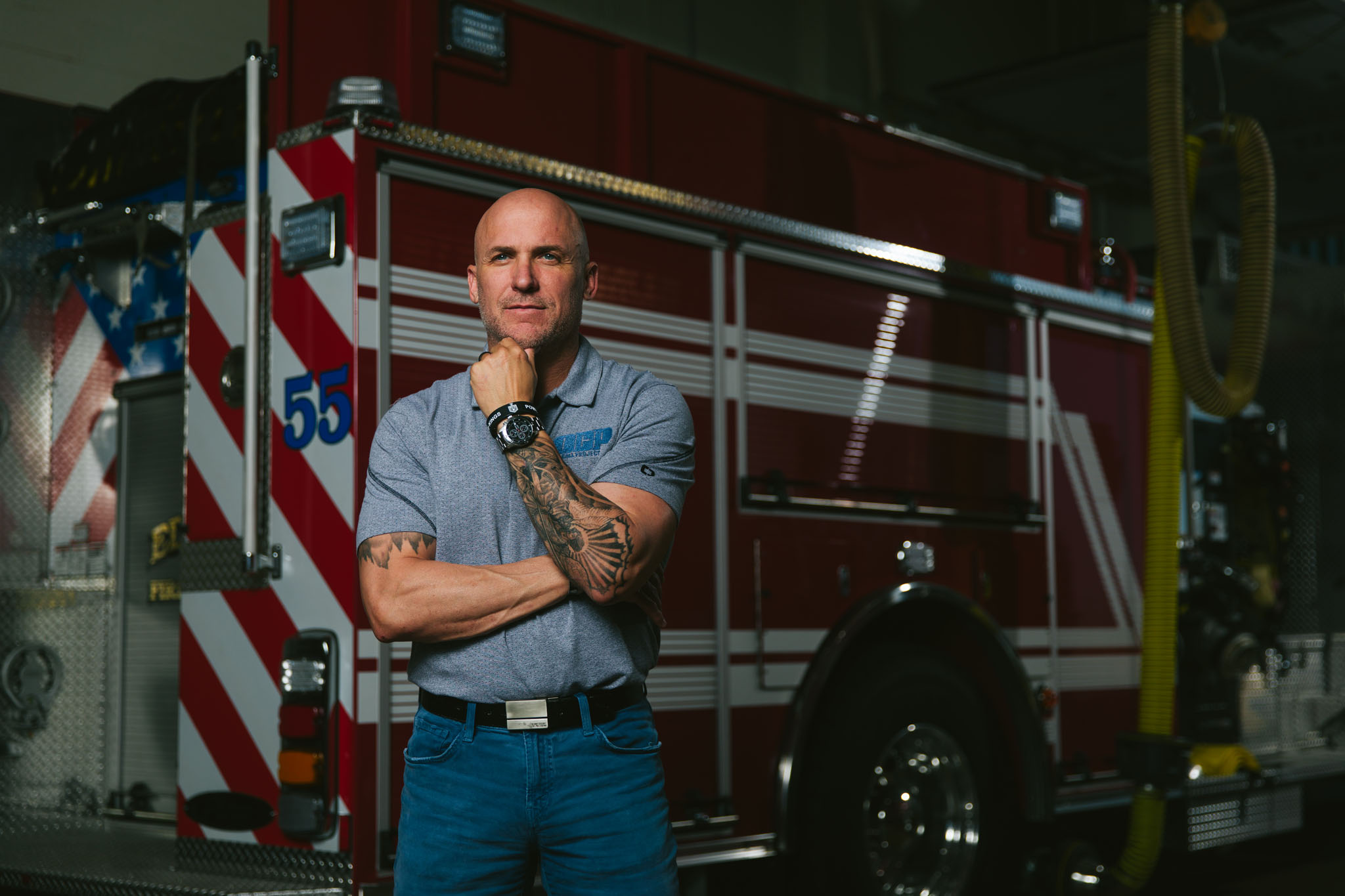 Firefighter with arms crossed standing in front of a fire engine in the station