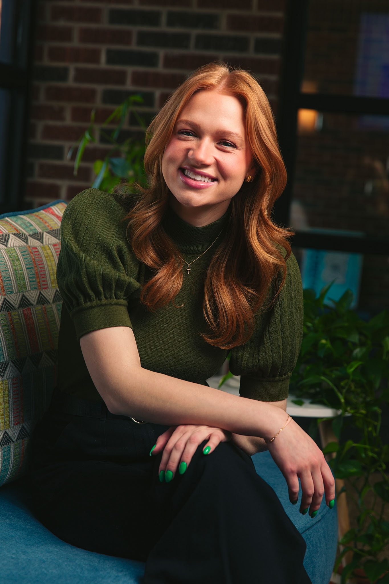 Smiling young woman with long red hair seated on a sofa in a green top