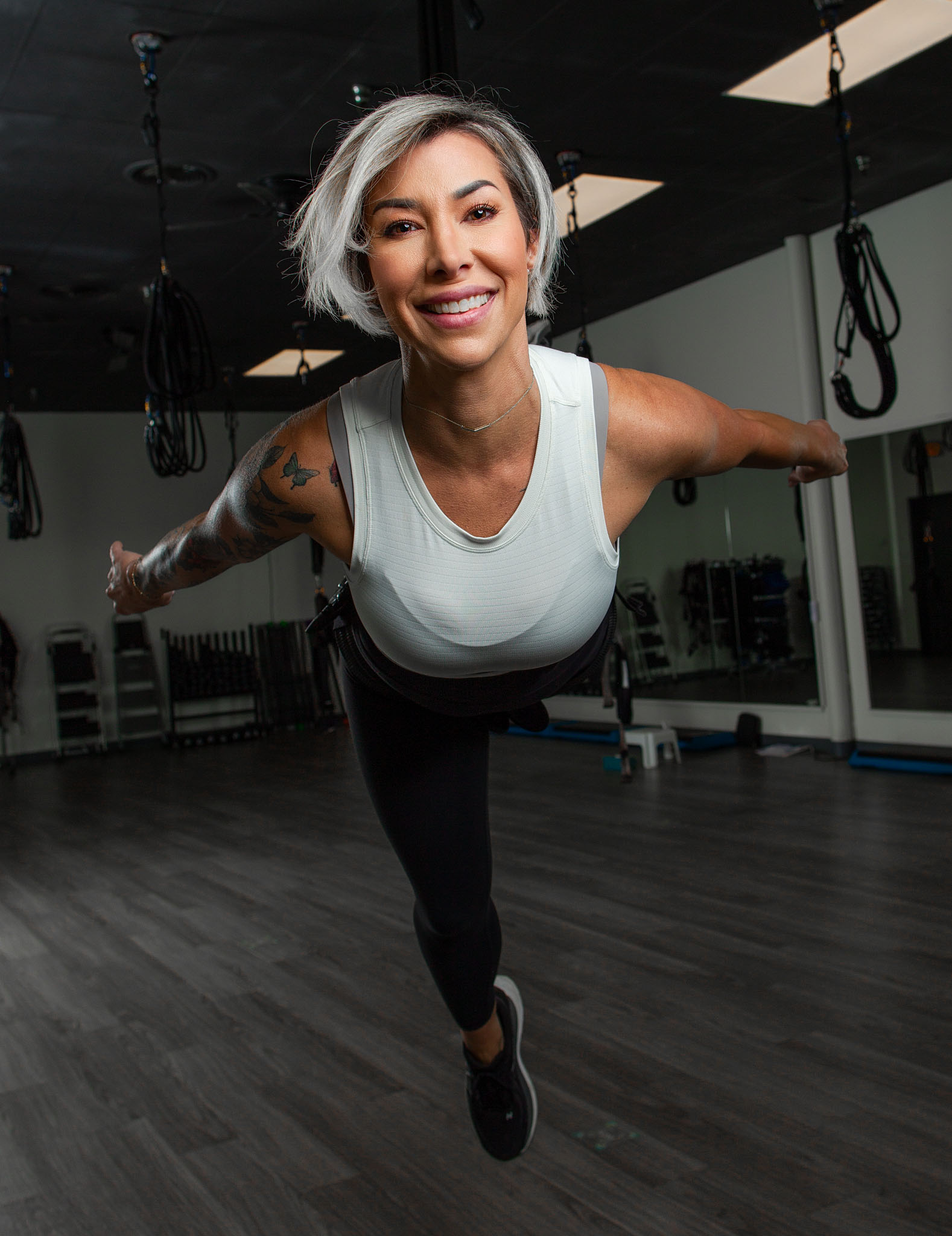 Smiling fitness instructor with silver hair balancing on one leg in a gym studio