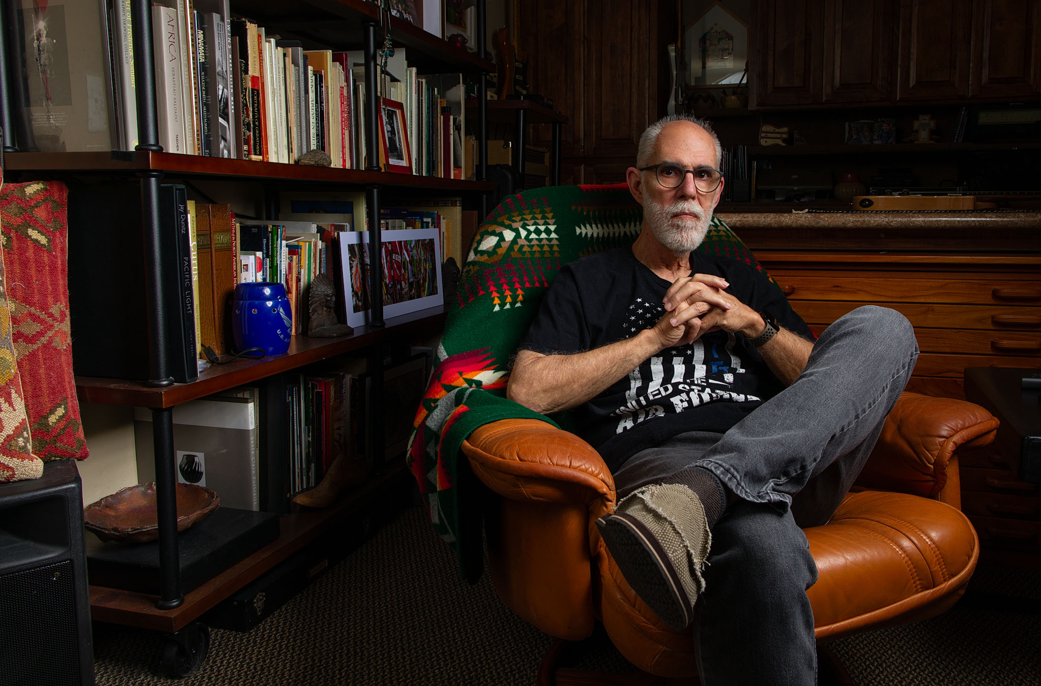 Man with a gray beard seated in a leather chair in front of bookshelves