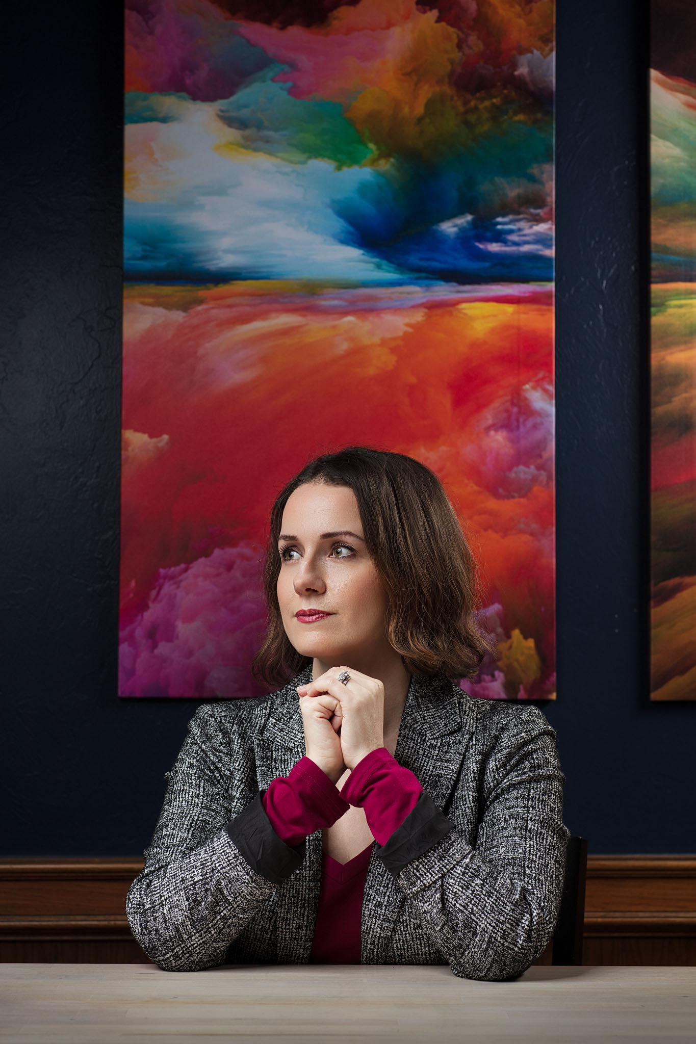 Woman in a tweed jacket seated at a table in front of a colorful abstract painting