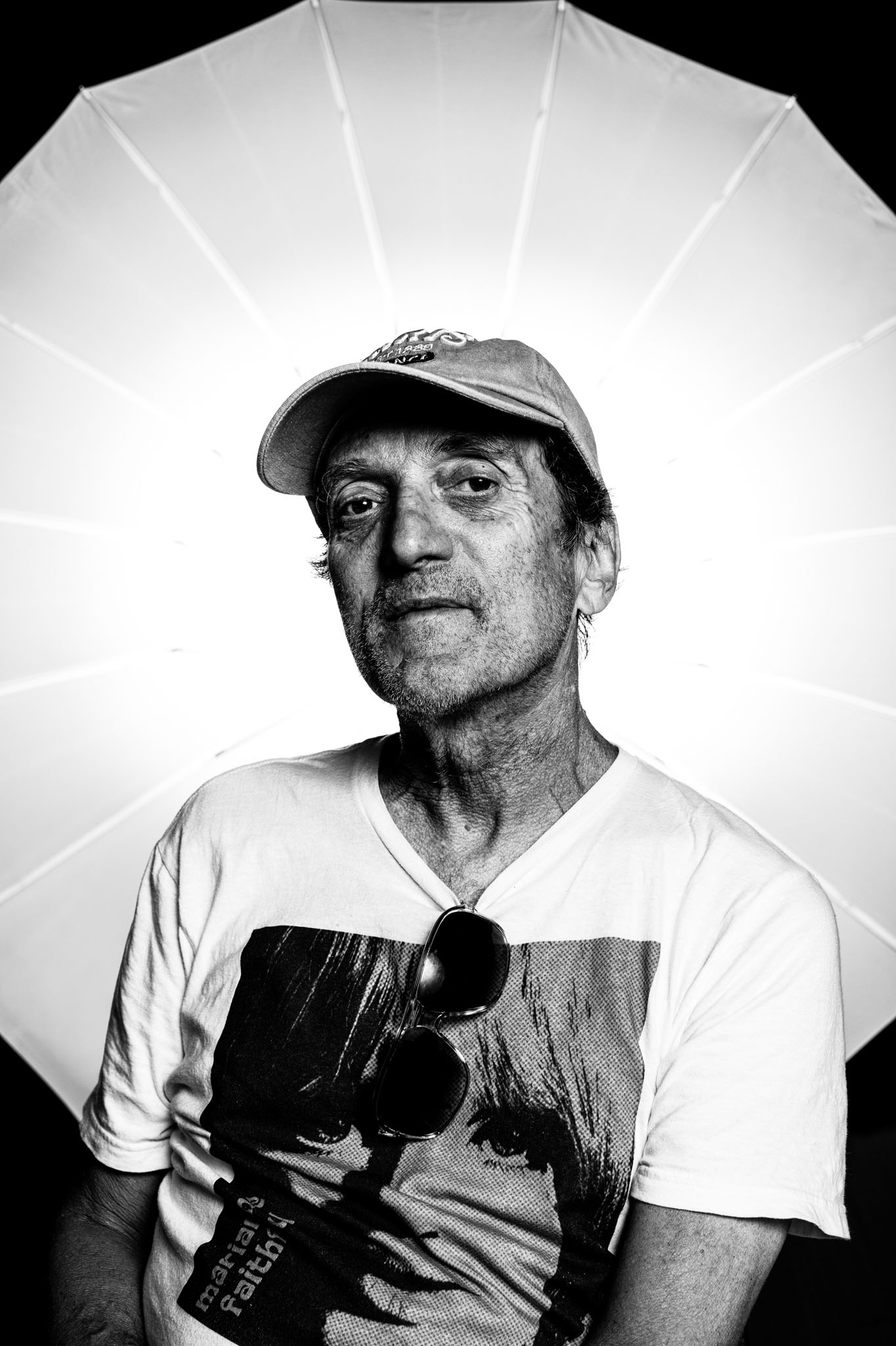 Black-and-white portrait of a weathered man in a ball cap in front of a white umbrella light