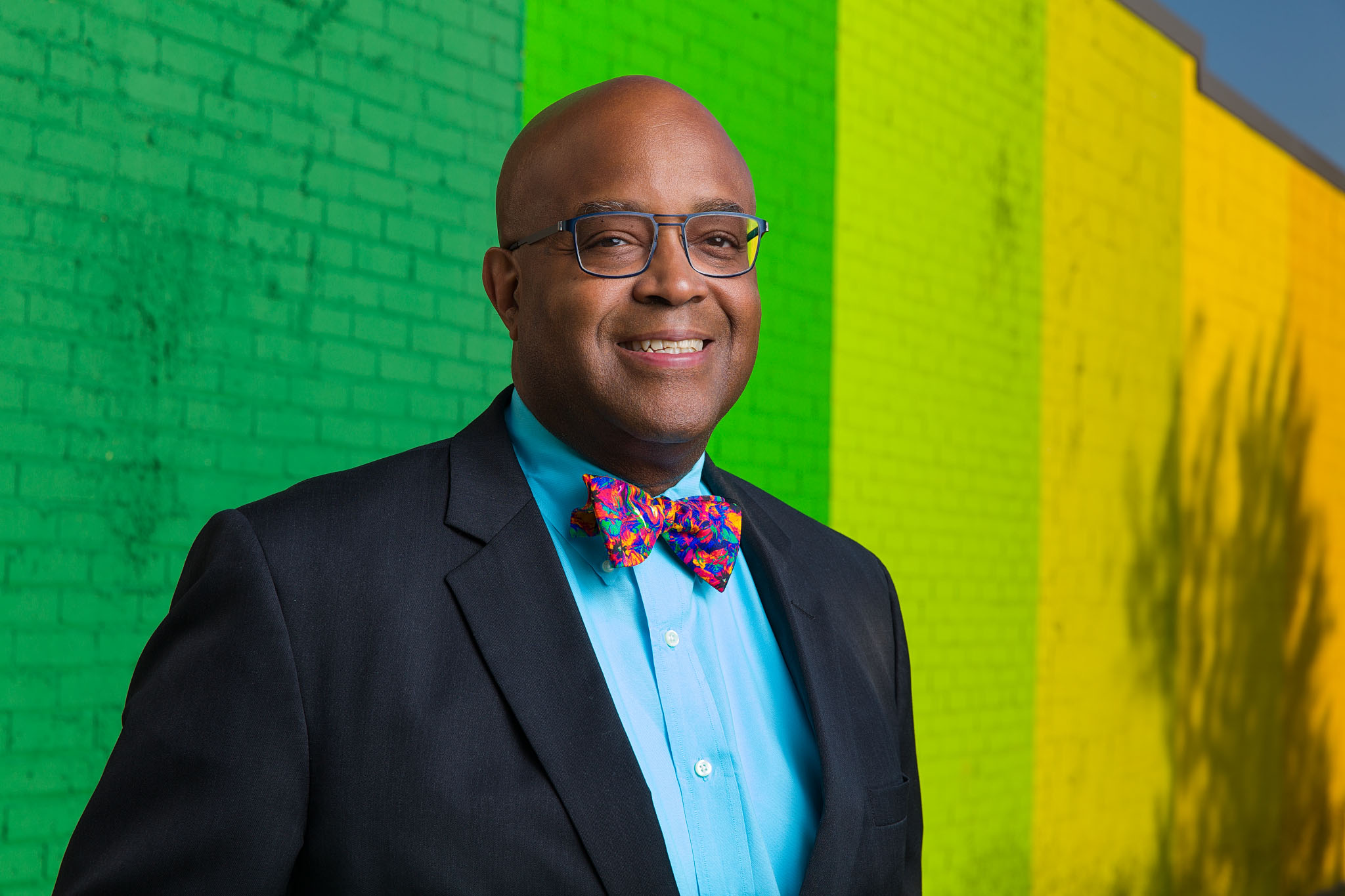 Smiling man in a suit and bow tie in front of a bright green and yellow painted wall