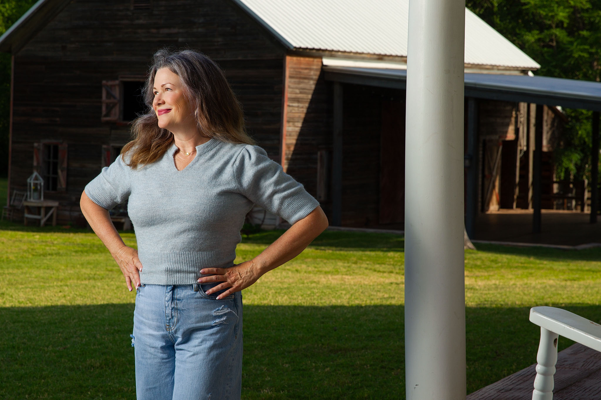 Woman with her hands on her hips standing in a grassy yard beside a porch