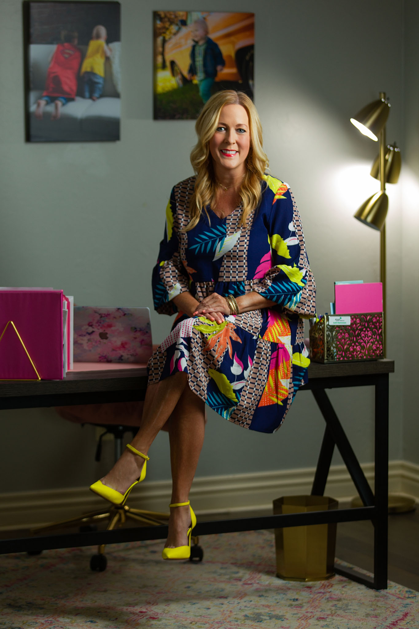 Woman in a colorful patterned dress seated on a desk in a styled office