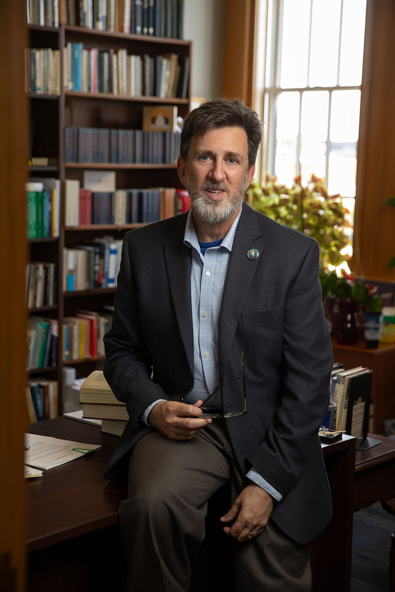 Man in a sport coat seated in a wood-paneled office lined with bookshelves