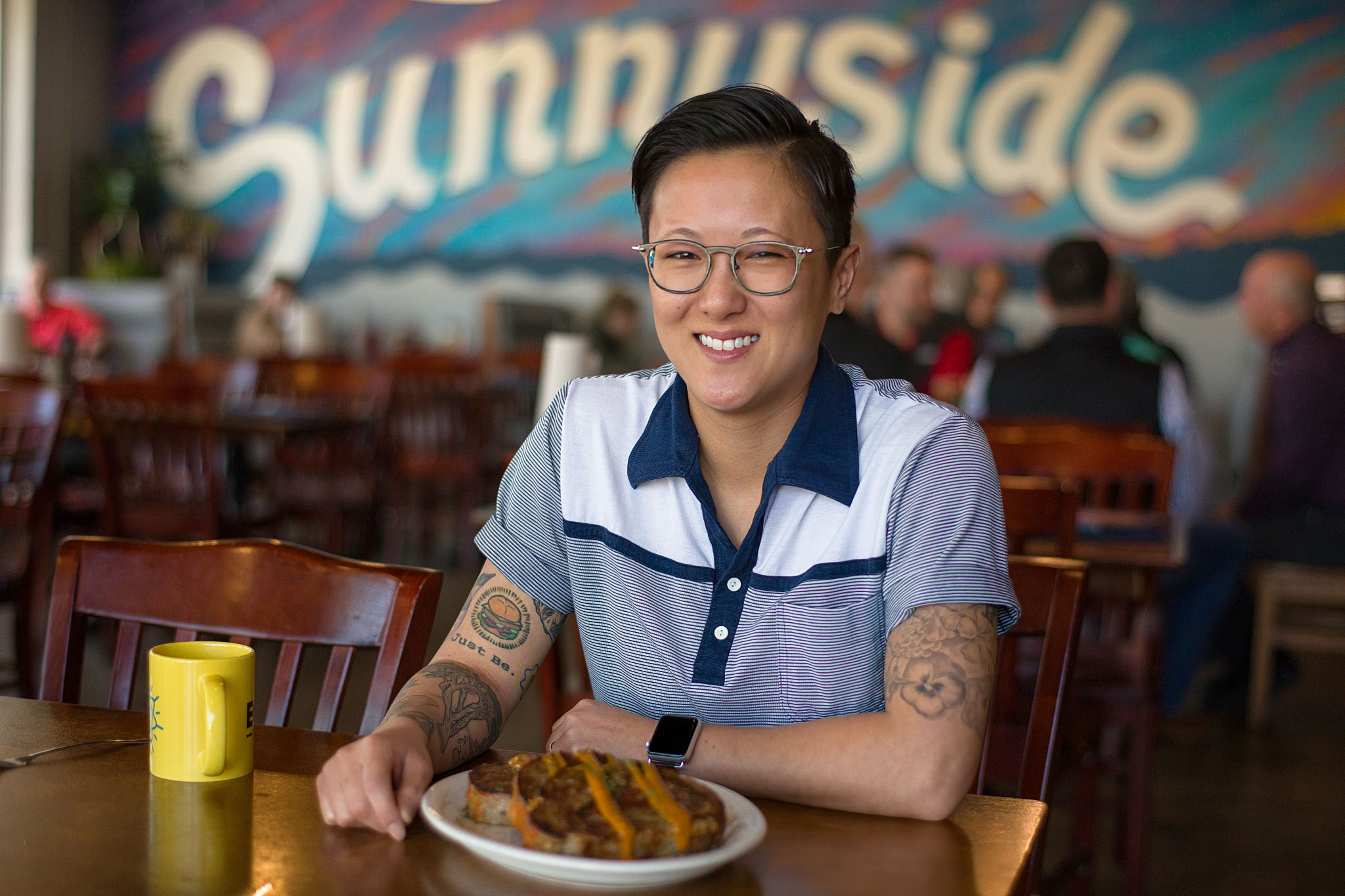 Smiling chef seated at a restaurant table with a plate of food beneath a painted mural