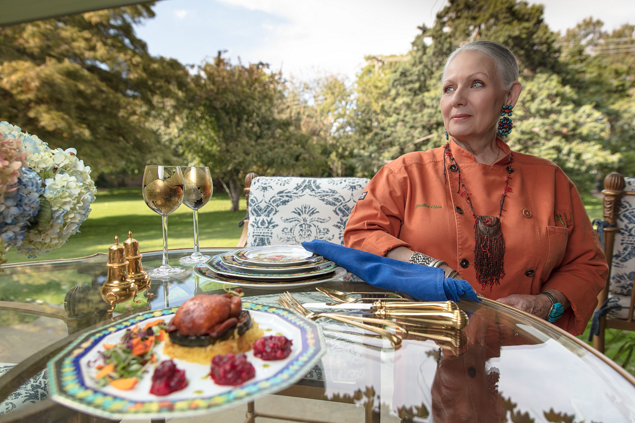 Chef seated at a garden table set with a plated meal and glasses of wine