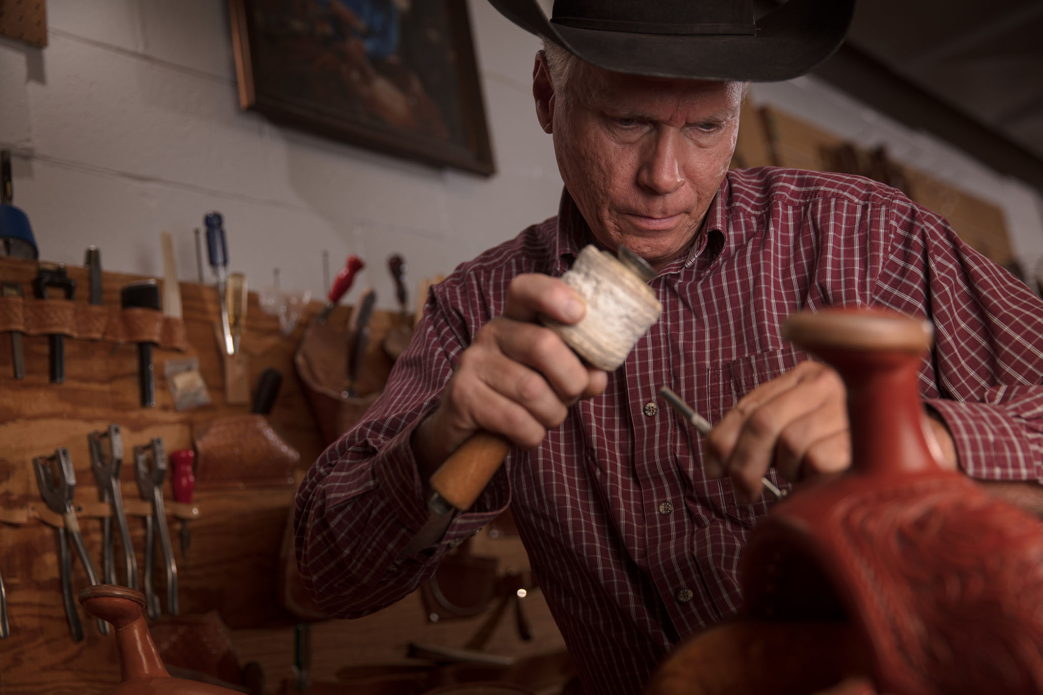 Saddle maker in a cowboy hat tooling leather on a saddle in his workshop