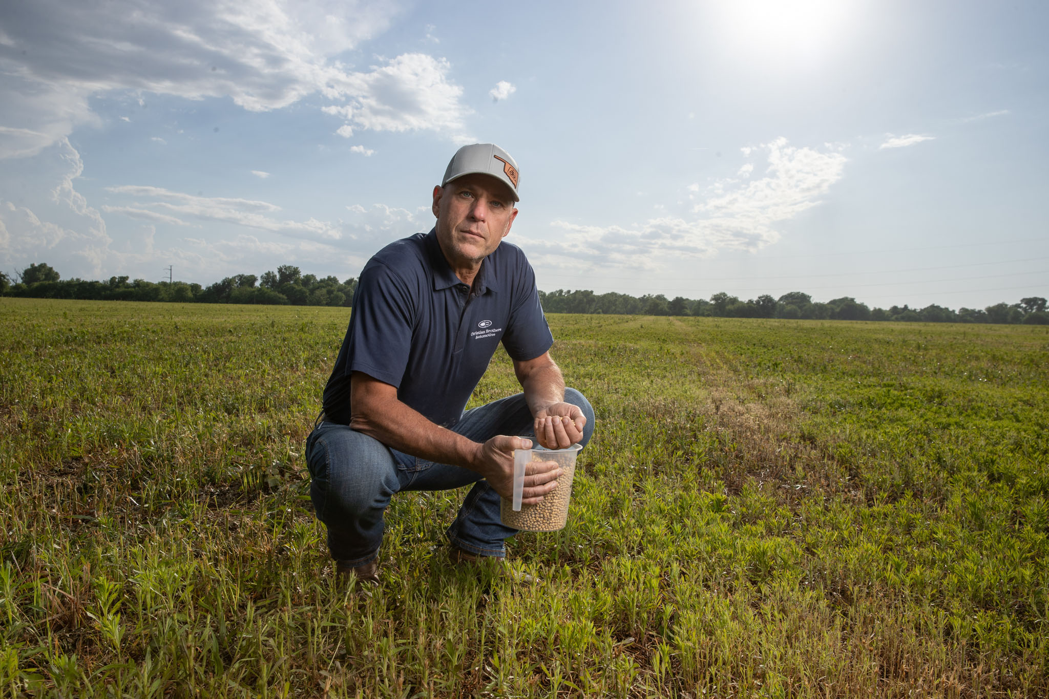 Farmer in a cap kneeling in a green field holding a bucket of seed
