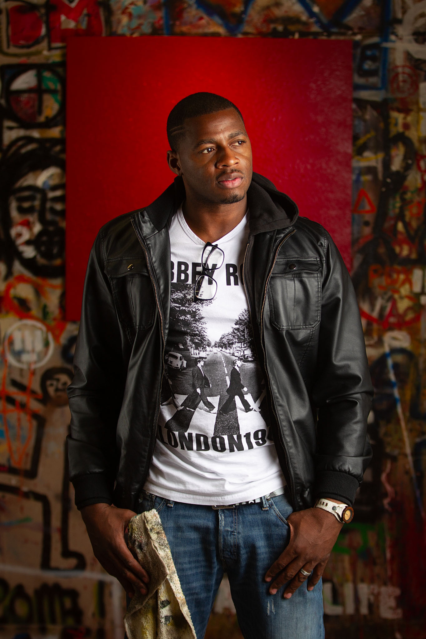 Young man in a black leather jacket in front of a red painted mural