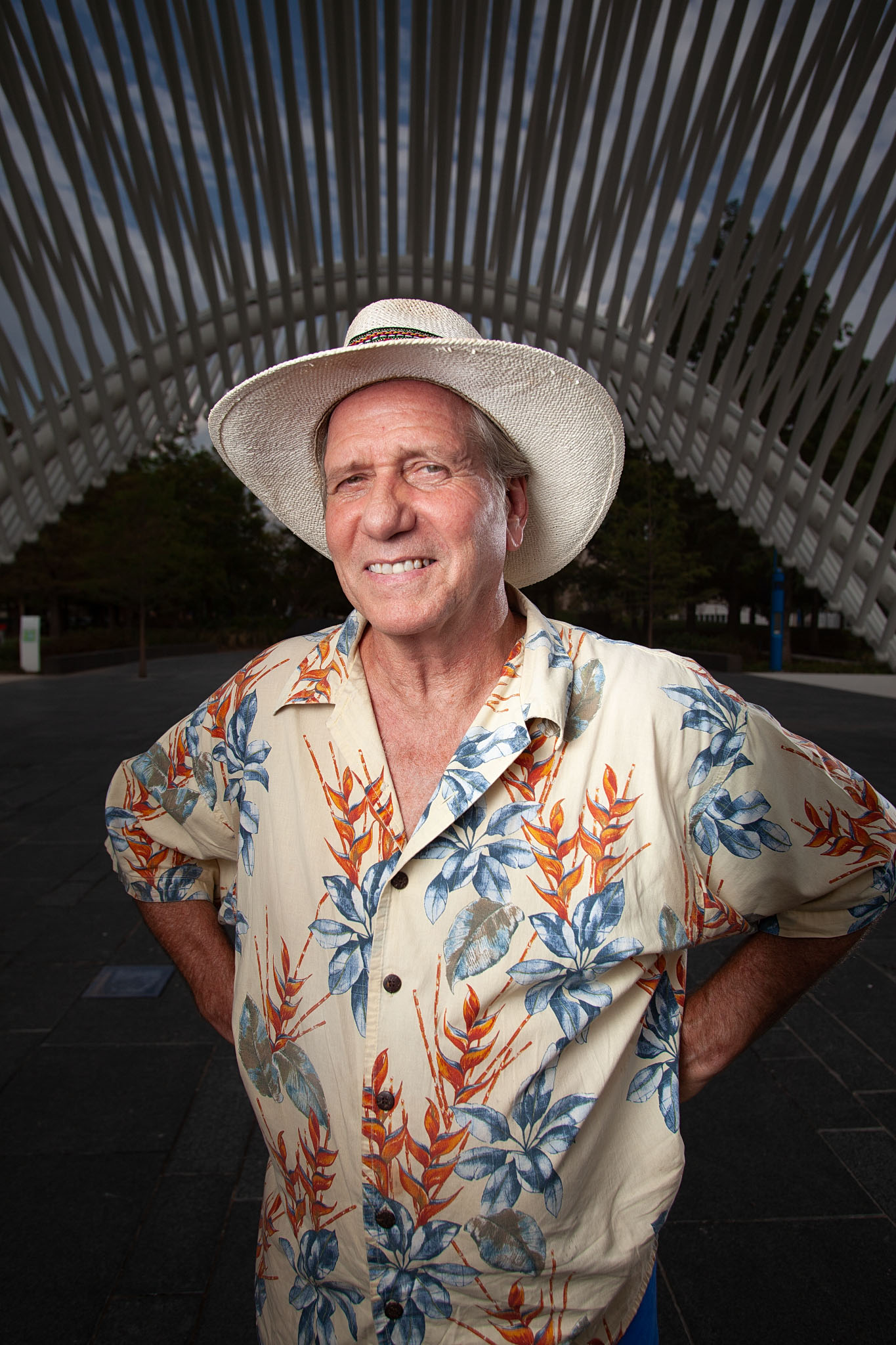 Smiling man in a white hat and floral shirt beneath an arched wooden structure
